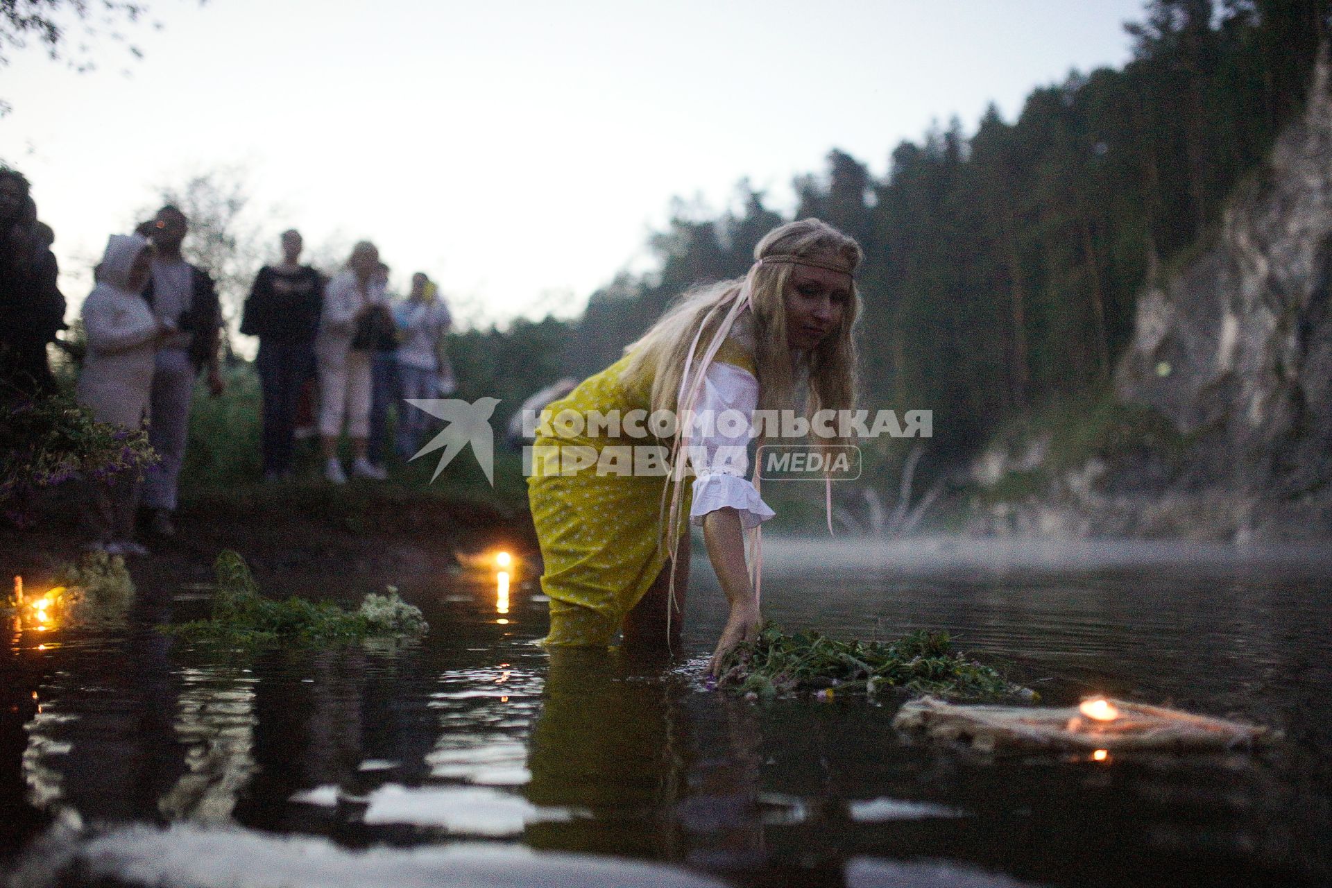 Участница празднования дня Ивана Купала спускает на воду венок