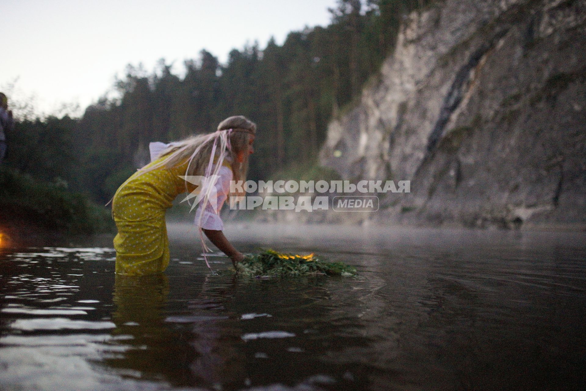 Участница празднования дня Ивана Купала спускает на воду венок