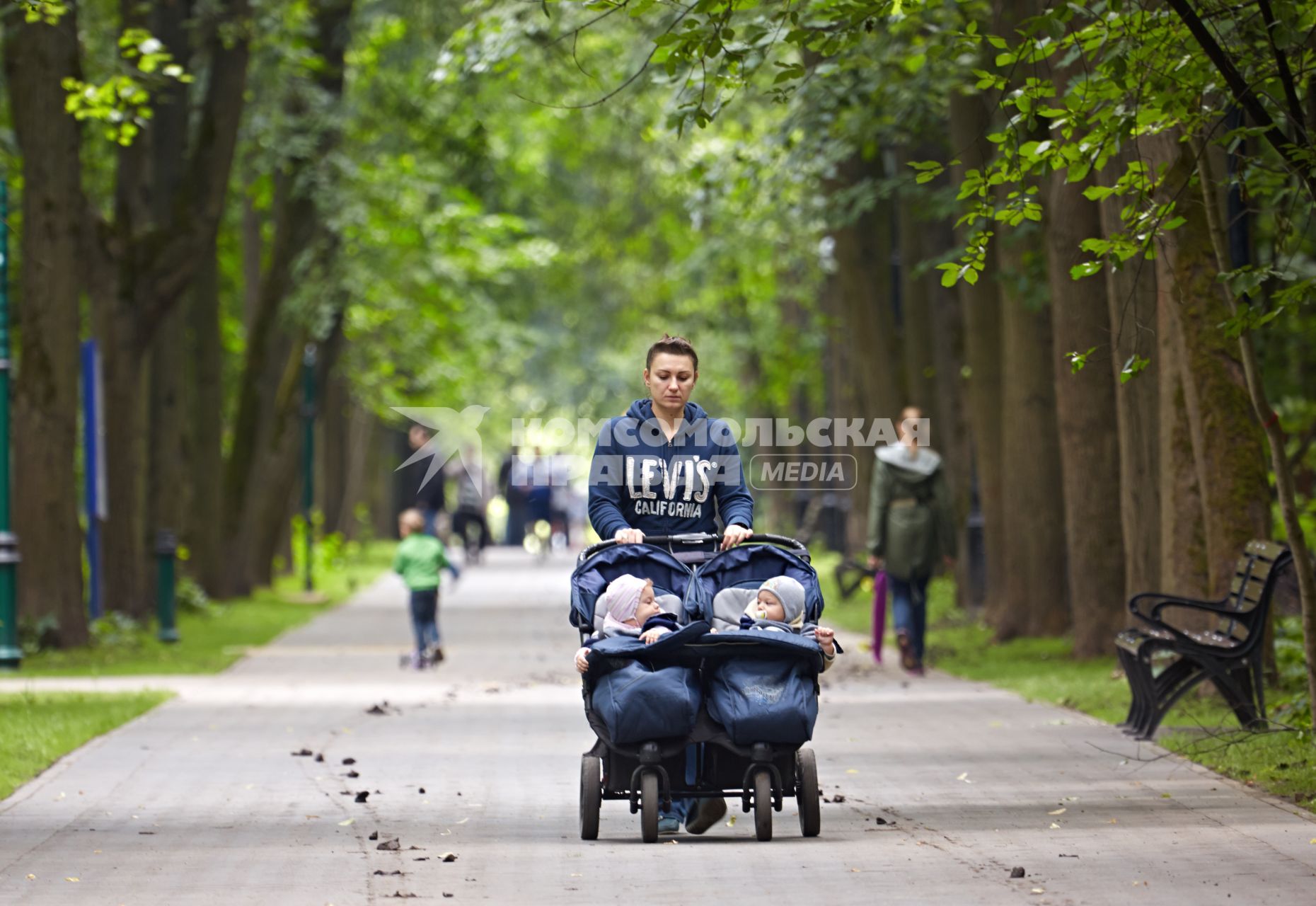 Женщина везет близнецов на детской коляске.