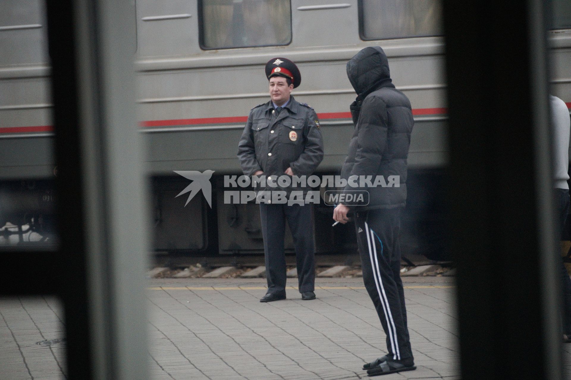 полицейский в куртке на вокзале рядом с курящим мужчиной