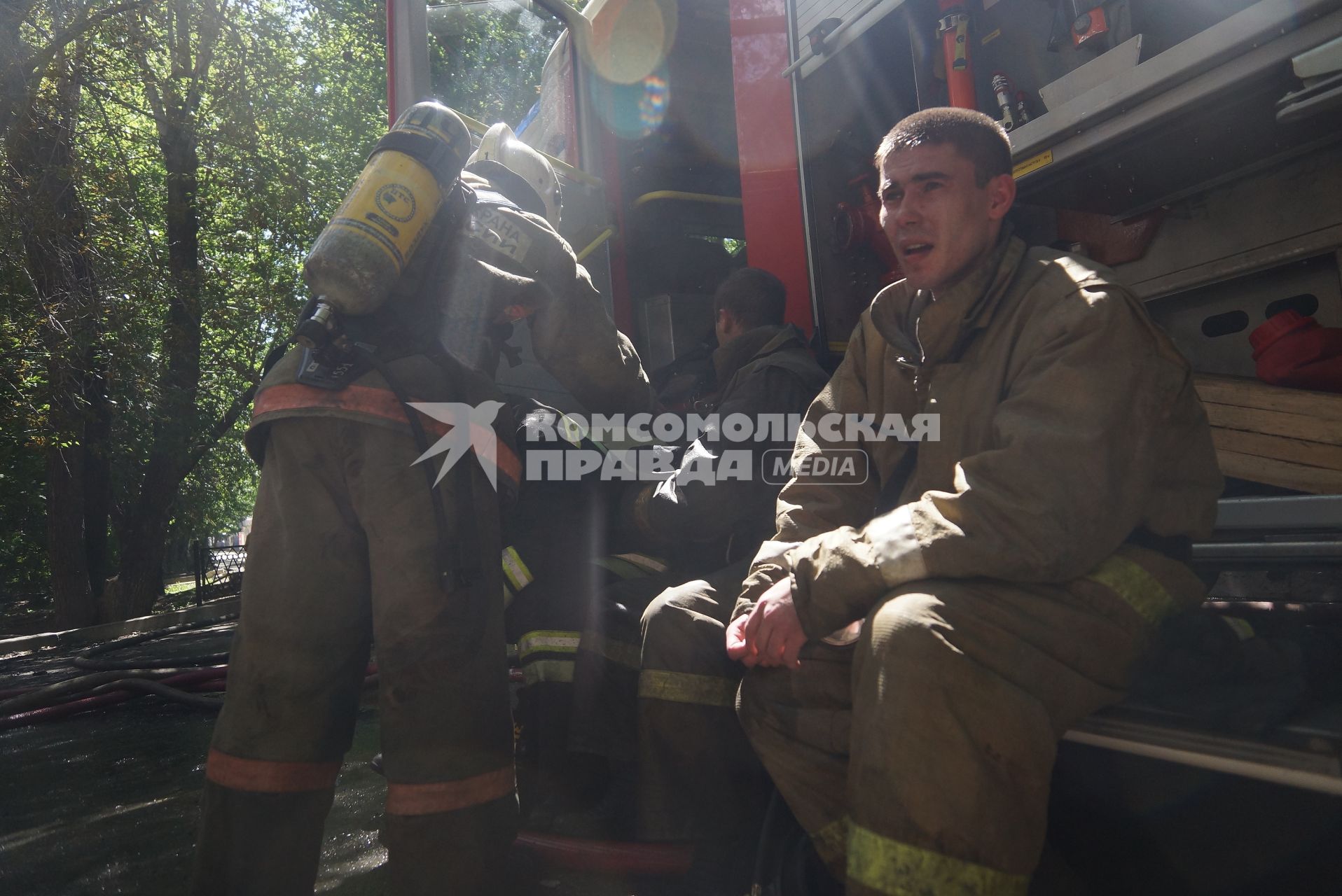 Пожарные отдыхают у машины во время пожара в доме