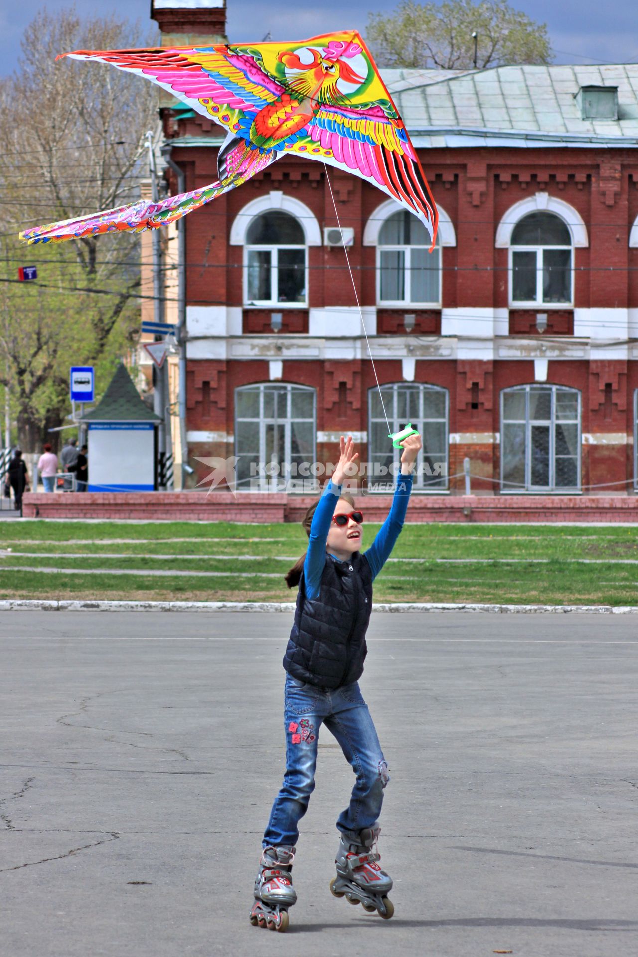 Ребенок пускает воздушного змея катаясь на роликах.