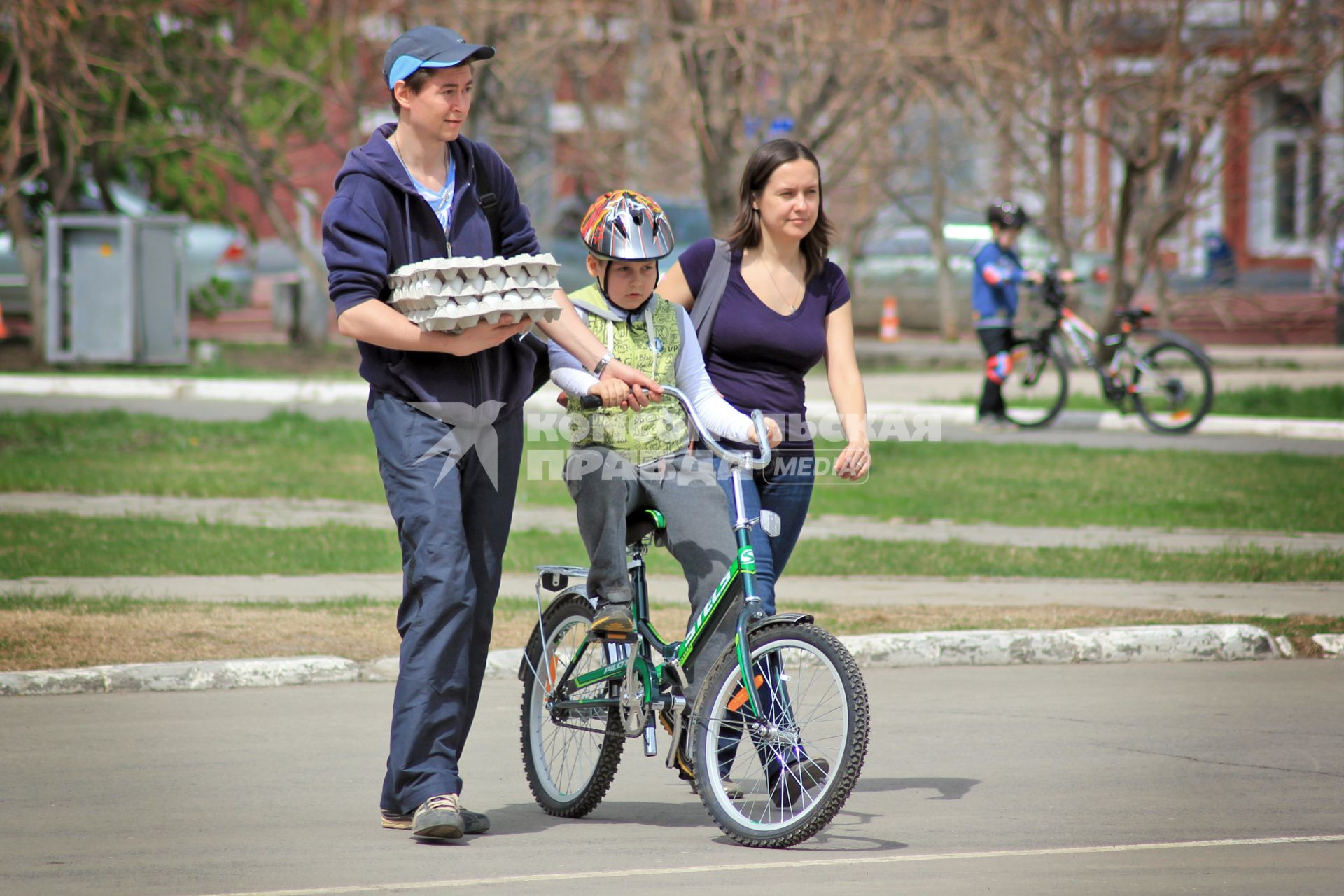 Семья учит ребенка кататься на велосипеде.