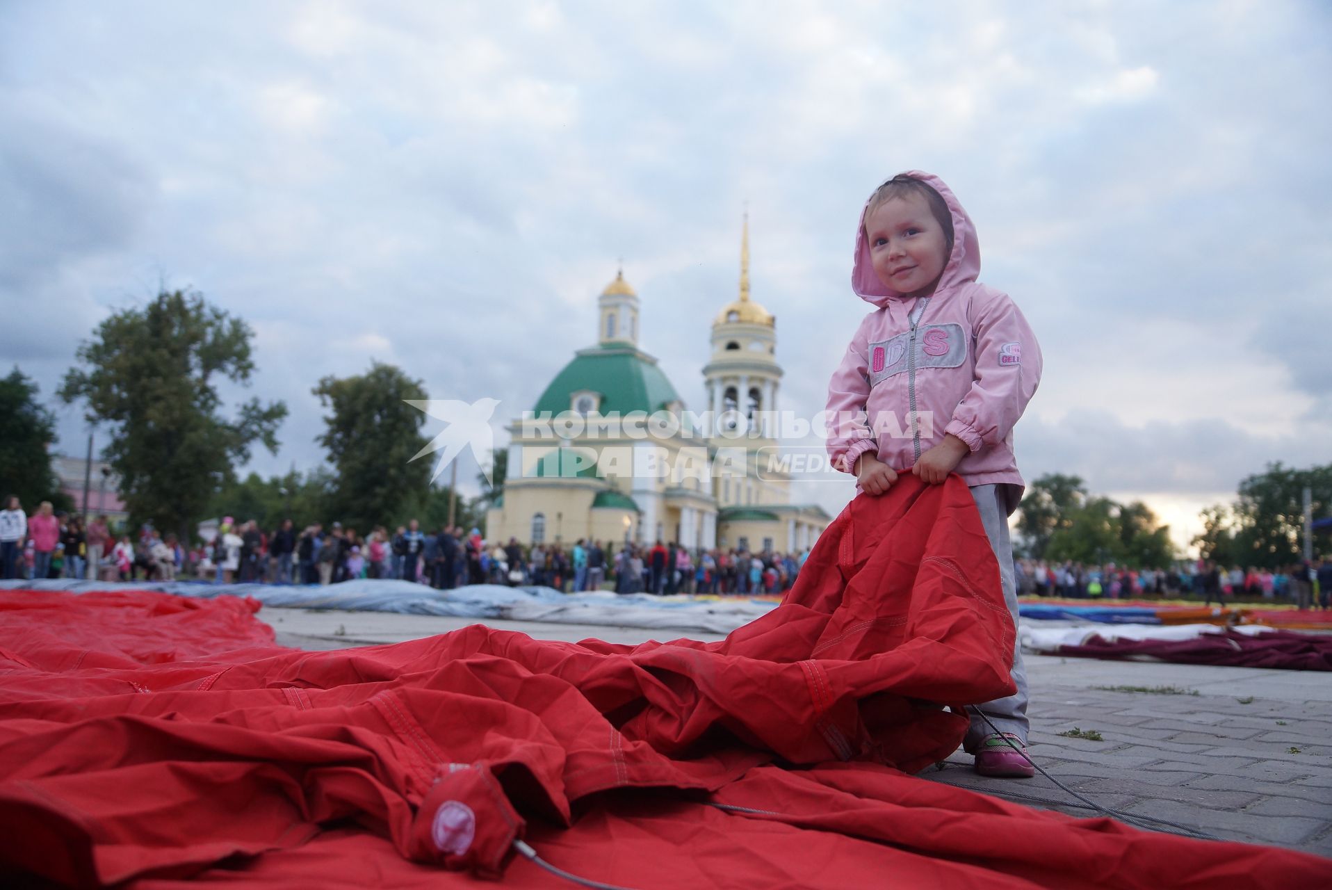 маленькачя девочка держит за край оболочку воздушного шара перед его наполнением на фестиале воздухоплавания \"небо на ладони\"  в Каменске-Уральском