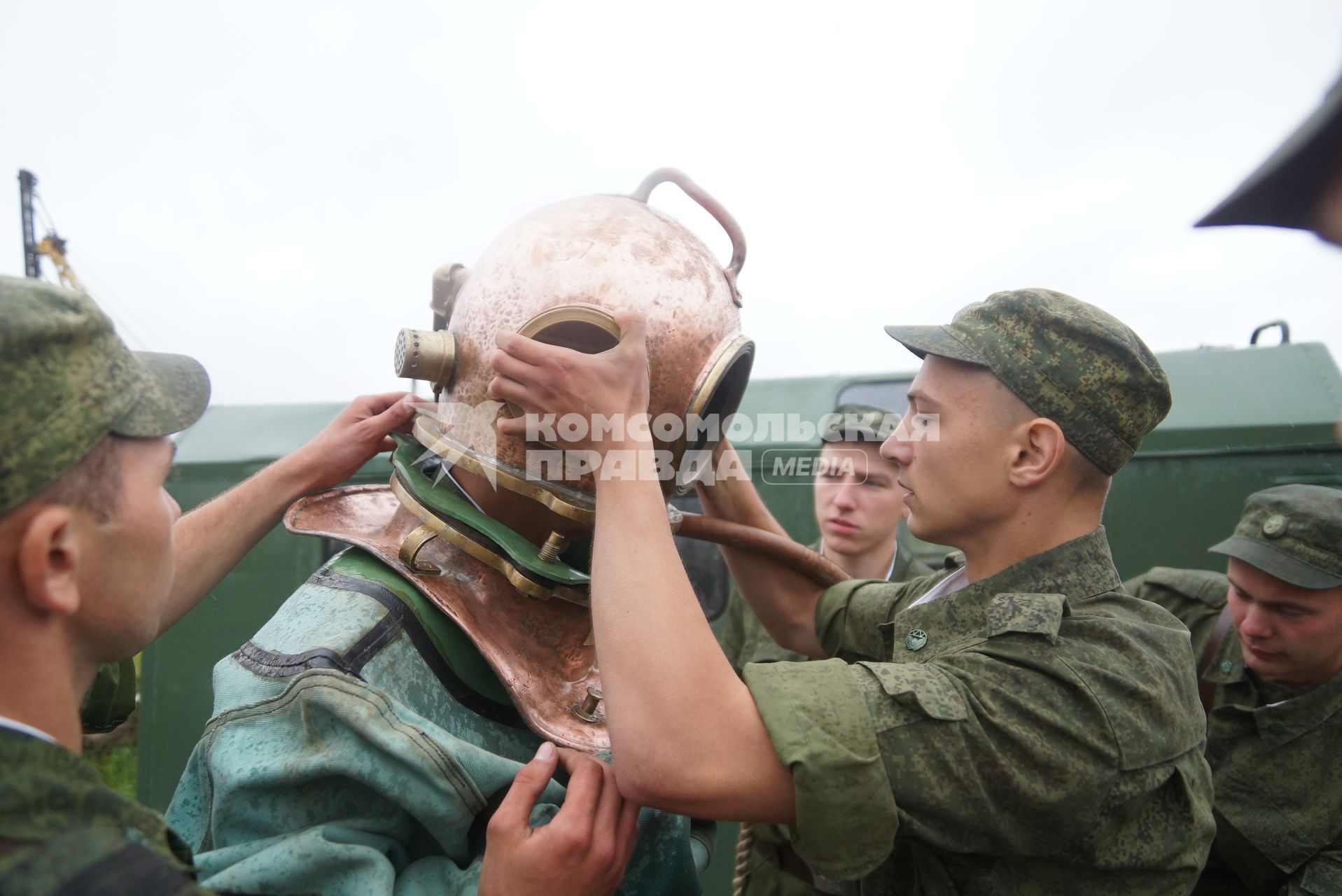 Солдат железнодорожных войск одевает тяжелый водолазный шлем на фодолаза