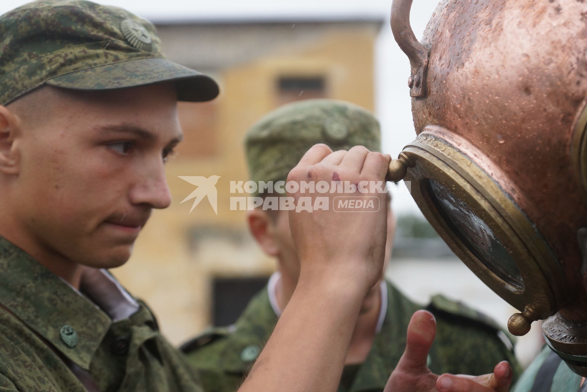 Солдат железнодорожных войск закрывает иллюминатор на тяжелом водолазном шлеме водолаза перед погружением