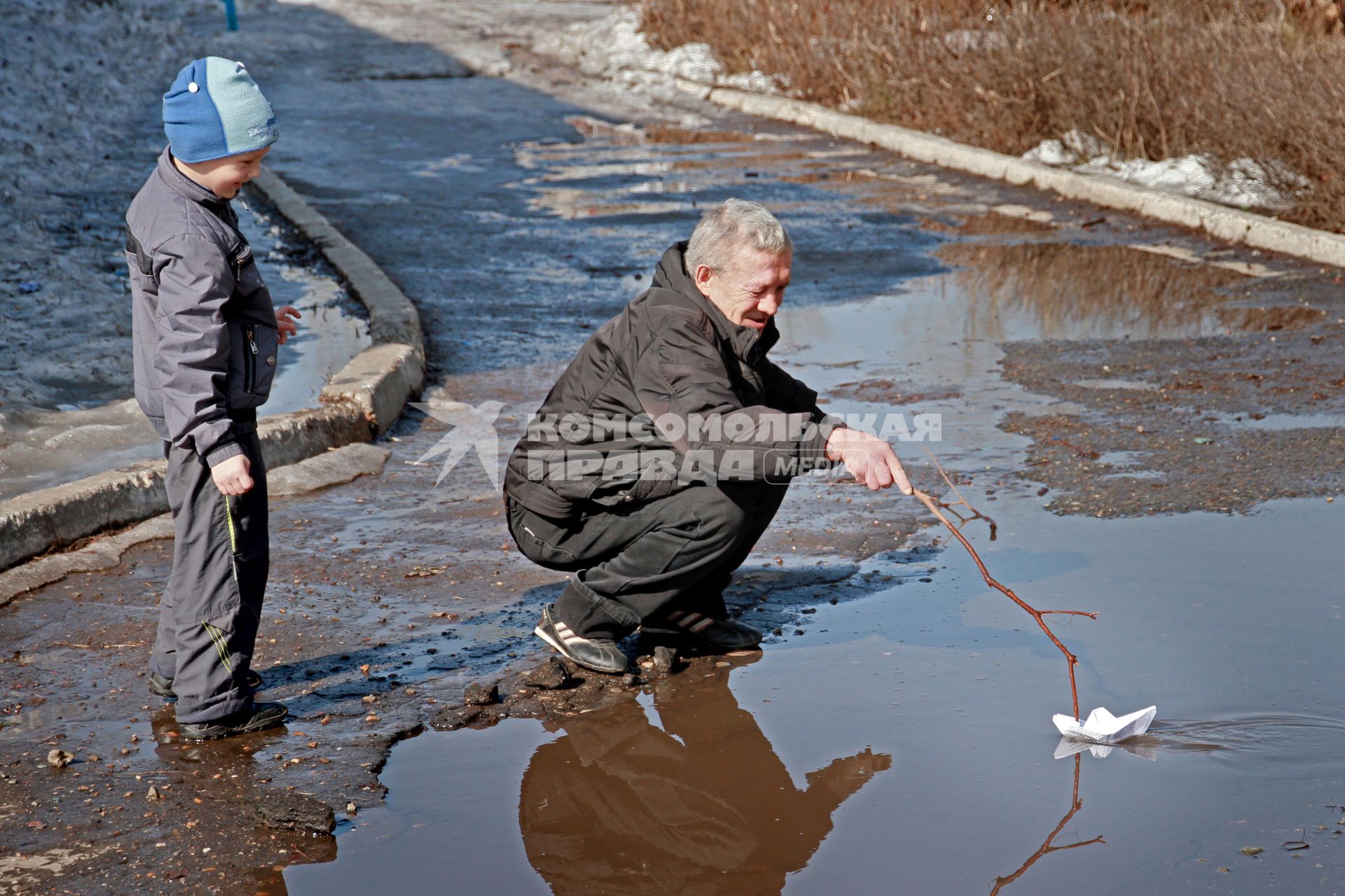 Дед с внуком пускают бумажный кораблик.