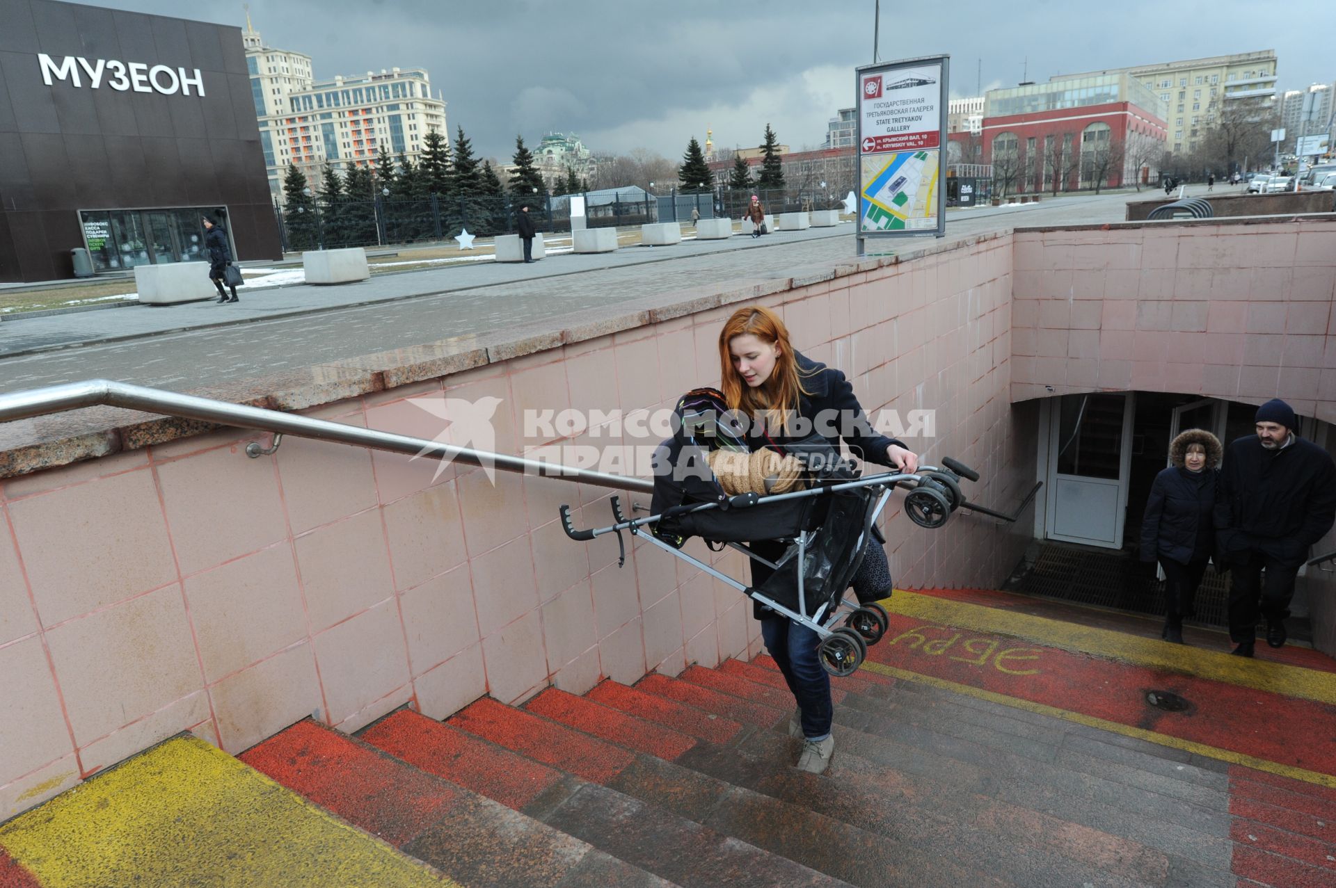 Женщина с детской коляской поднимается по лестнице.