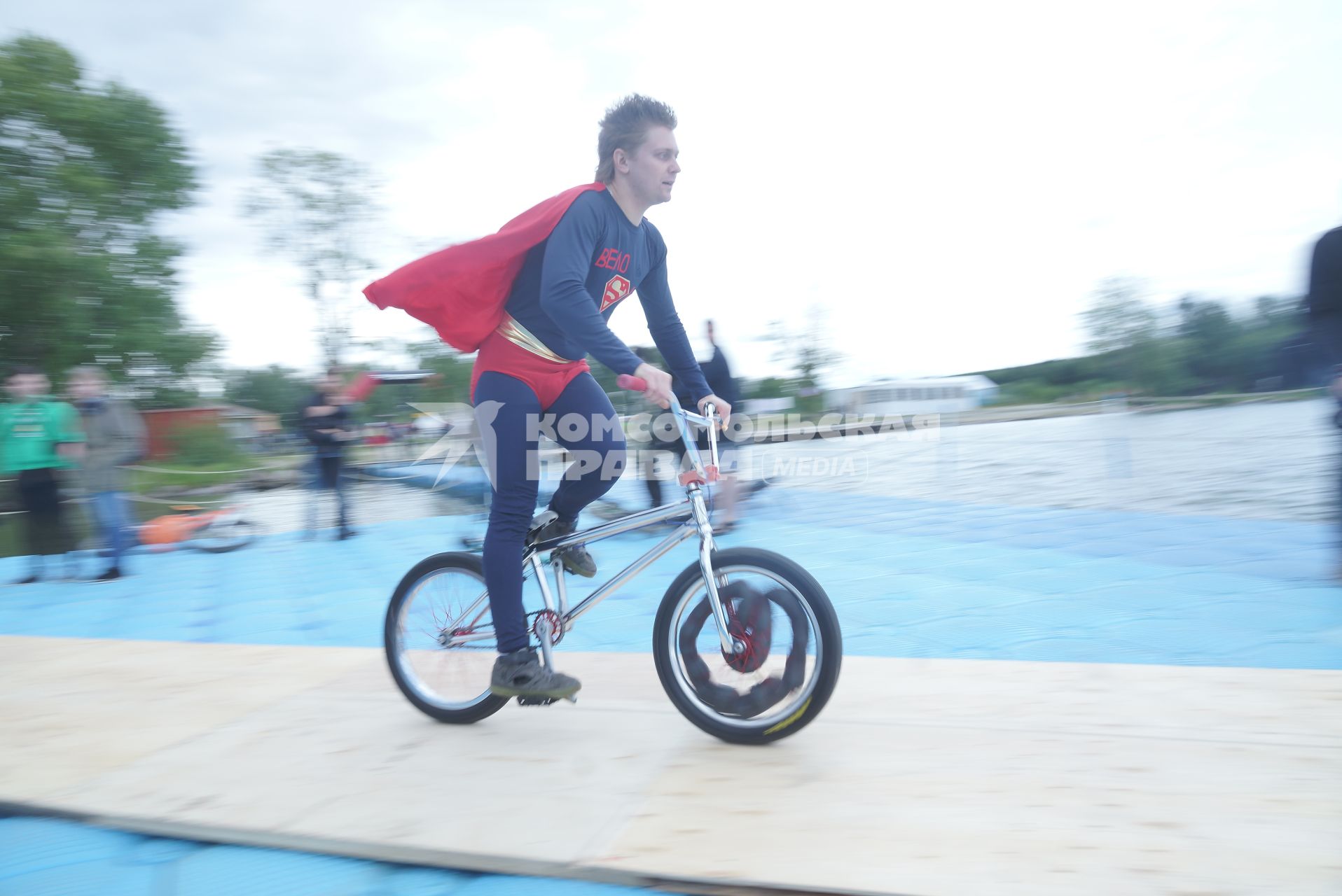 Прыжки на велосипедах в воду Bicycle live fest, парень в костюме супермена едет на велосипеде к трамплину