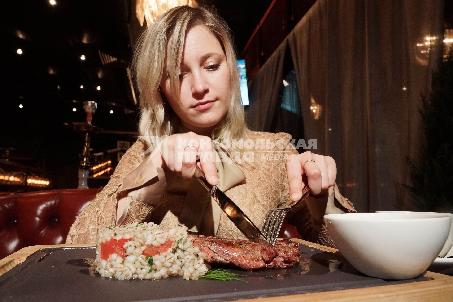 Девушка в ресторане  \"Огонек\" в Екатеринбурге, который ввел санкционное меню., ест отбивную из говяжей вырезки с перлотто и клюквеным соусом