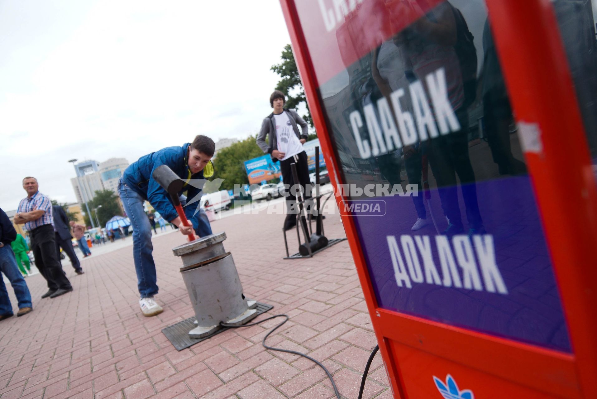 Мужчина в день физкультурника бьет кувалдой по наковальне силомера