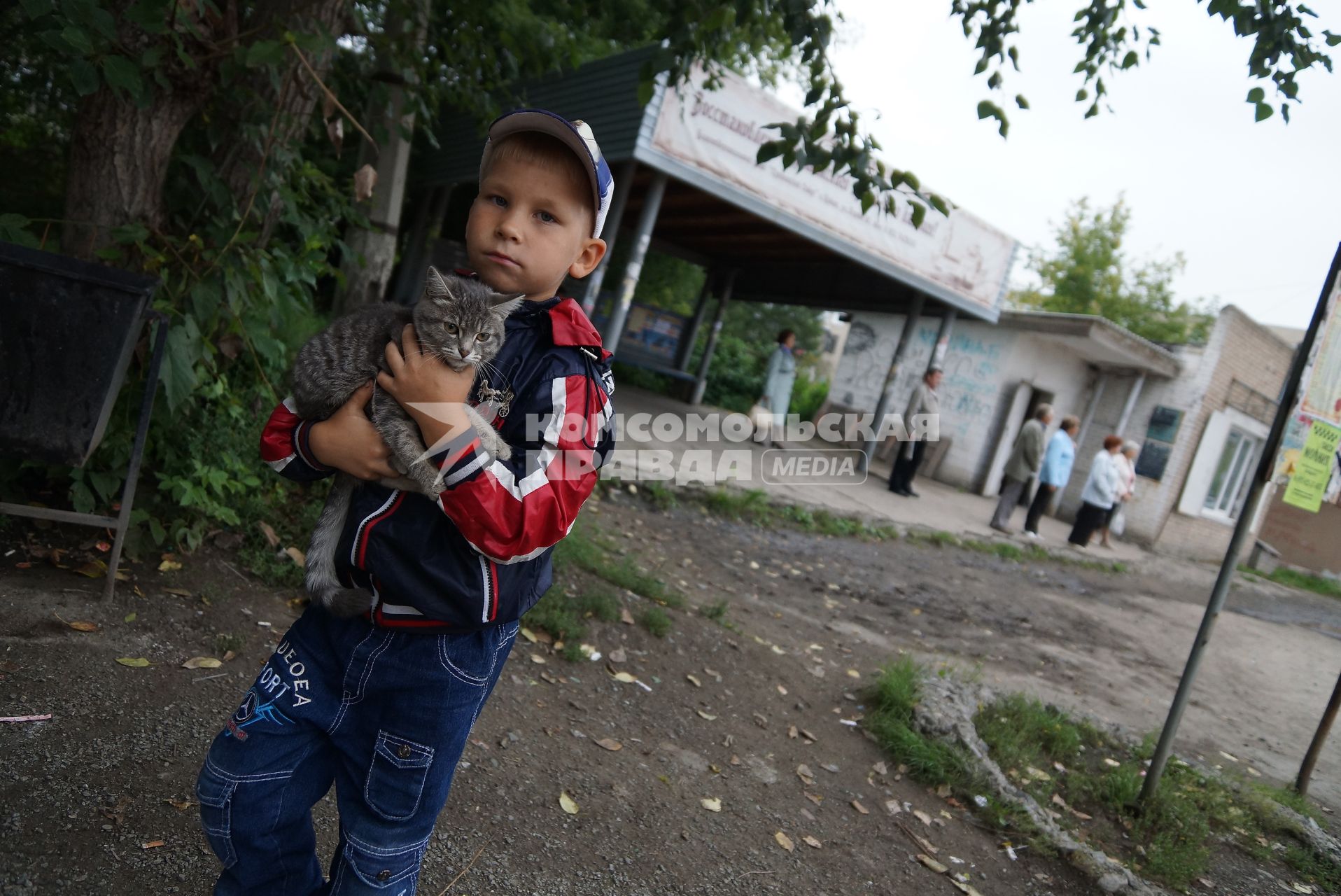 мальчик держит на руках кошку у остановки общественного транспорта в городе Ирбит
