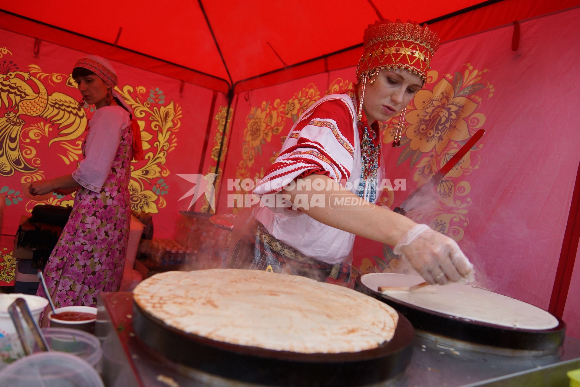 девушка с традиционном русском наряде печет блины на Ирбитской ярмарке