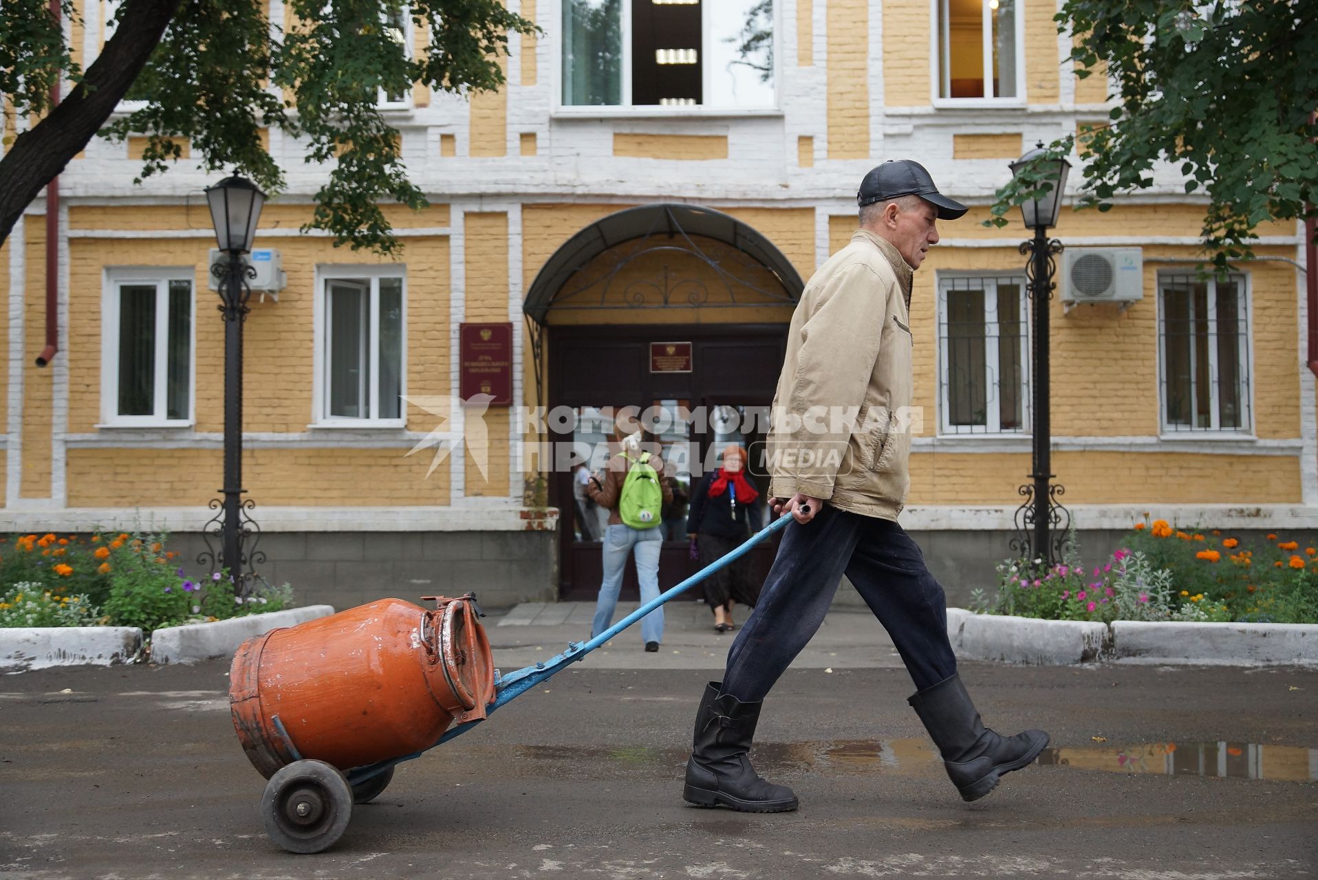 мужчина проходит с тележкой с металлическим бидон мимо здания администрации в городе Ирбит