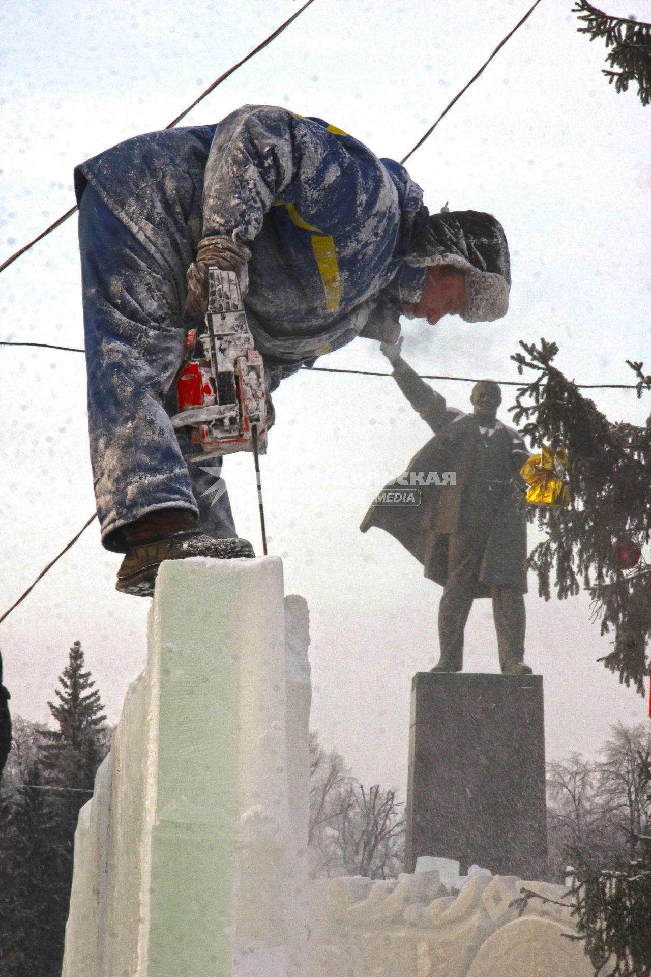 Строительство ледового городка в Уфе. Рабочий пилит лед напротив памятника В.И. Ленину.