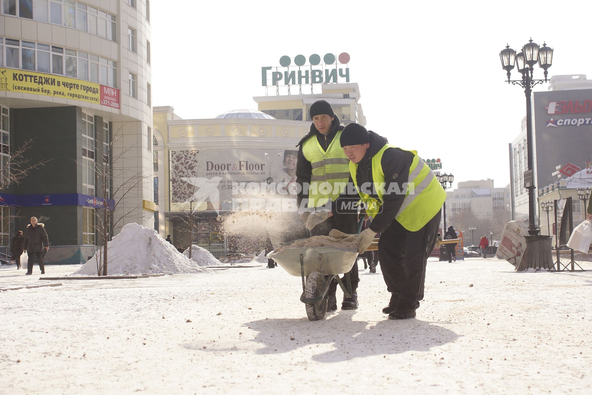 дворники разбрасывают антигололедную смесь по тротуару