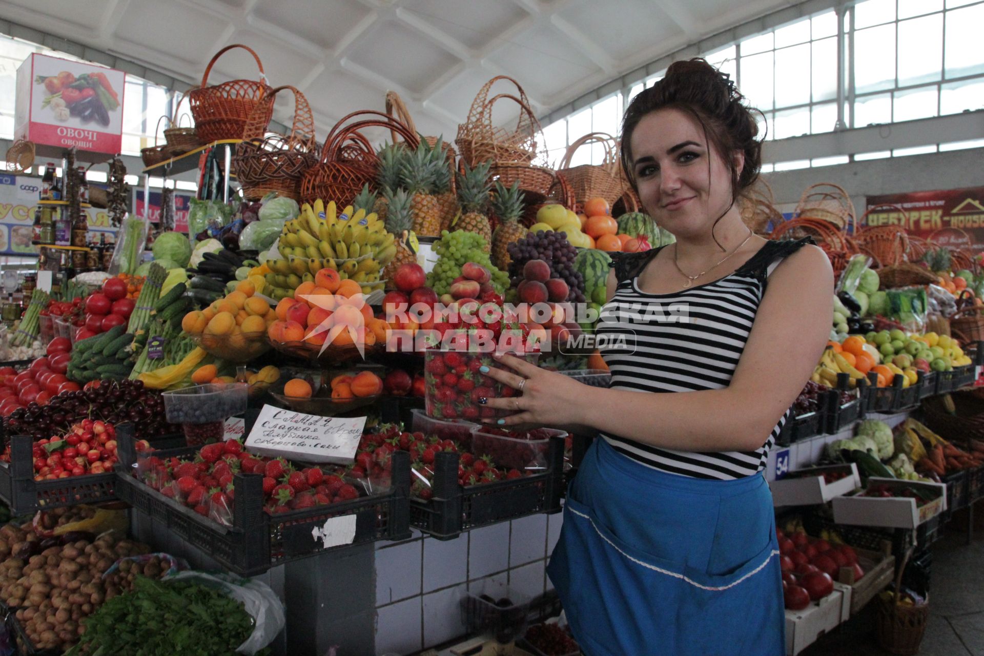 Девушка-продавец на рынке в Крыму с клубникой в руках.