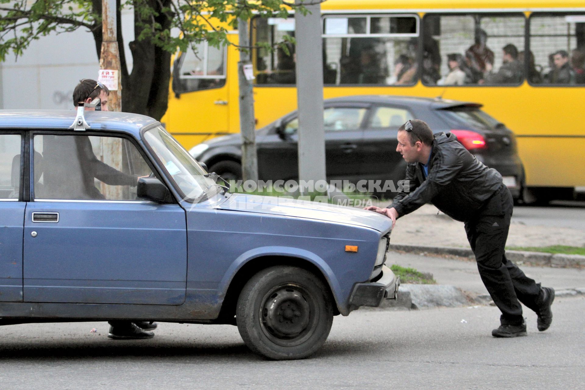 Мужчина толкает заглохший автомобиль.