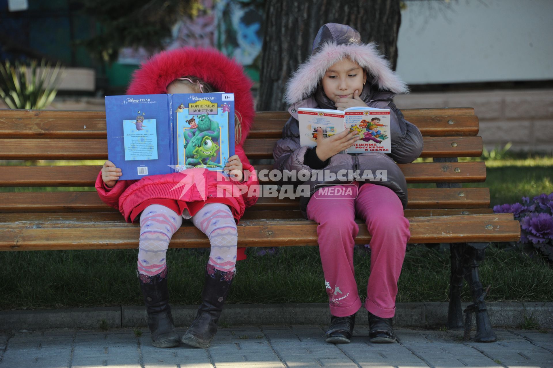 Девочки читают книги на скамейке.