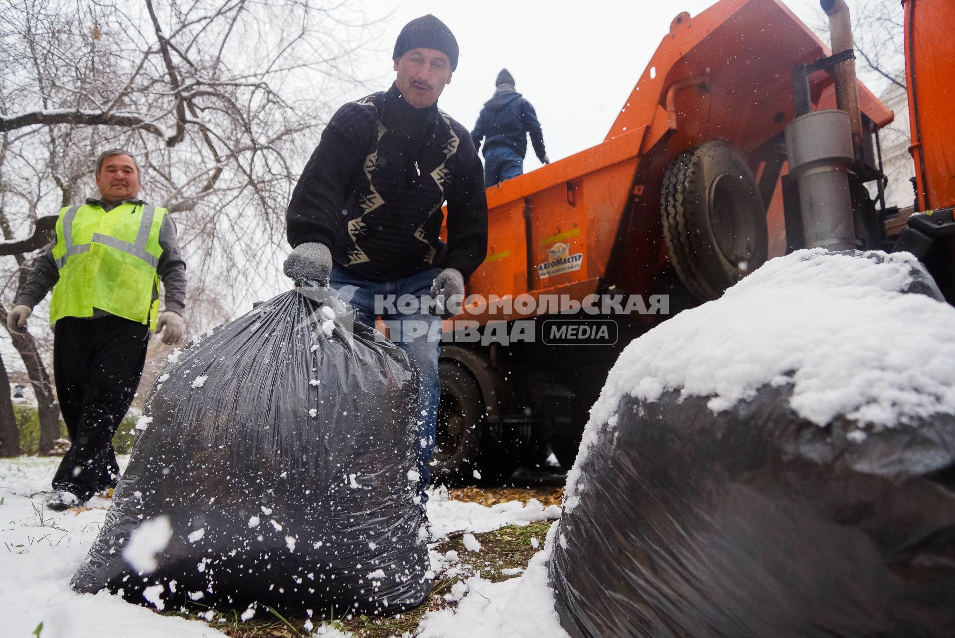 Коммунальные рабочие грузят мешки с опавшей листвой в кузов грузовика