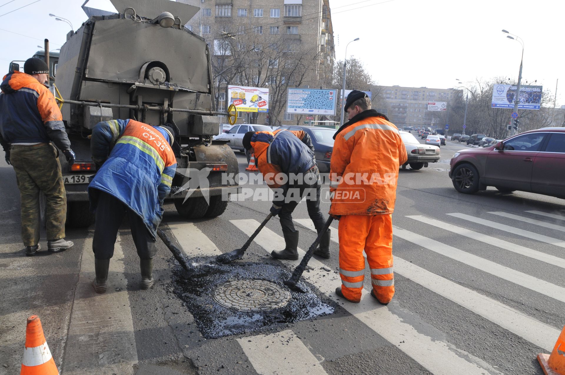 Рабочие укладывают асфальт вокруг люка на дороге.