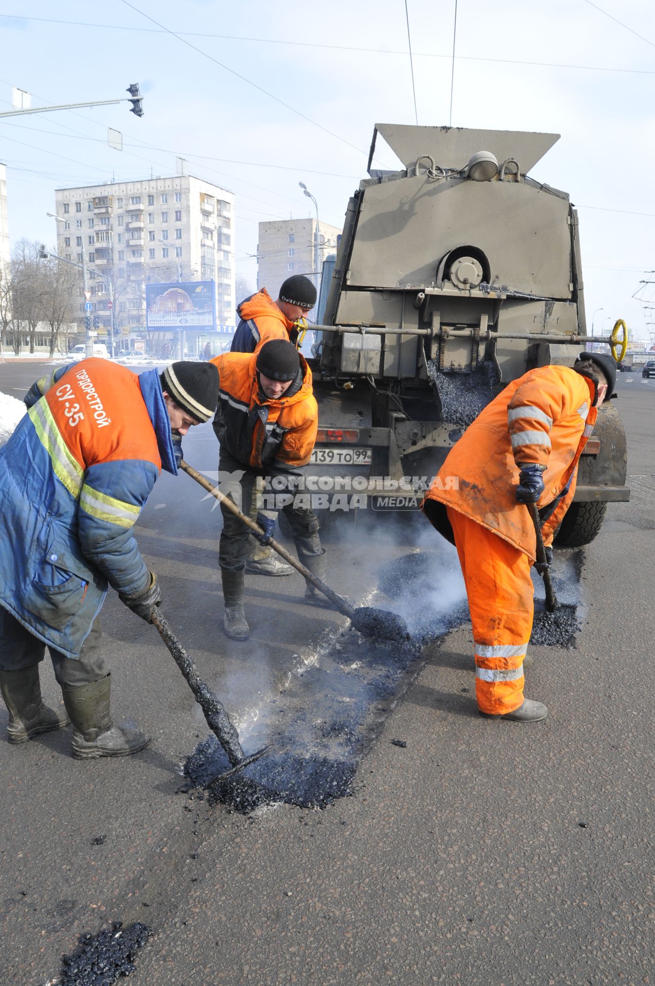 Рабочие укладывают асфальт вокруг люка на дороге.