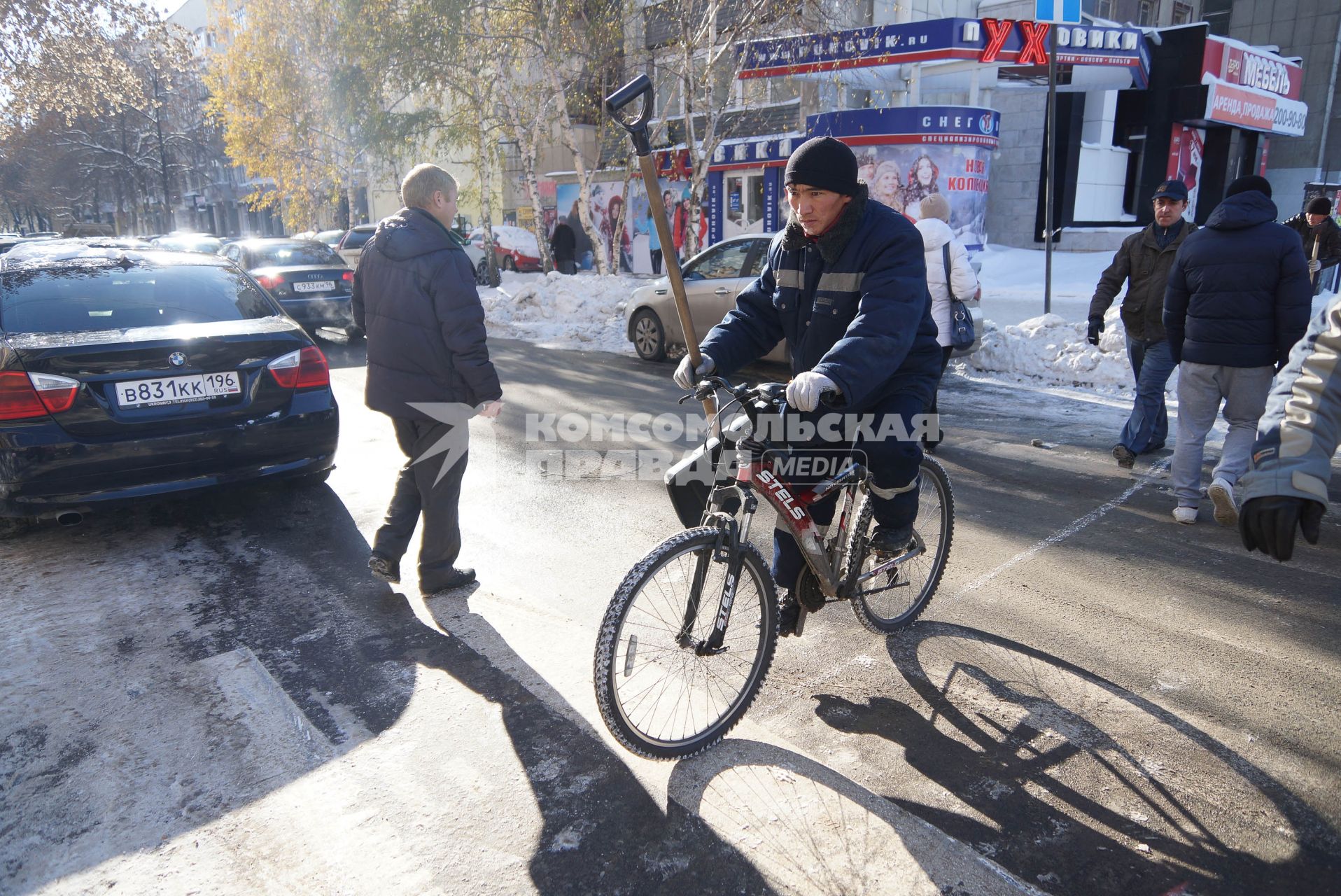 Дворник с лопатой едет на велосипеде