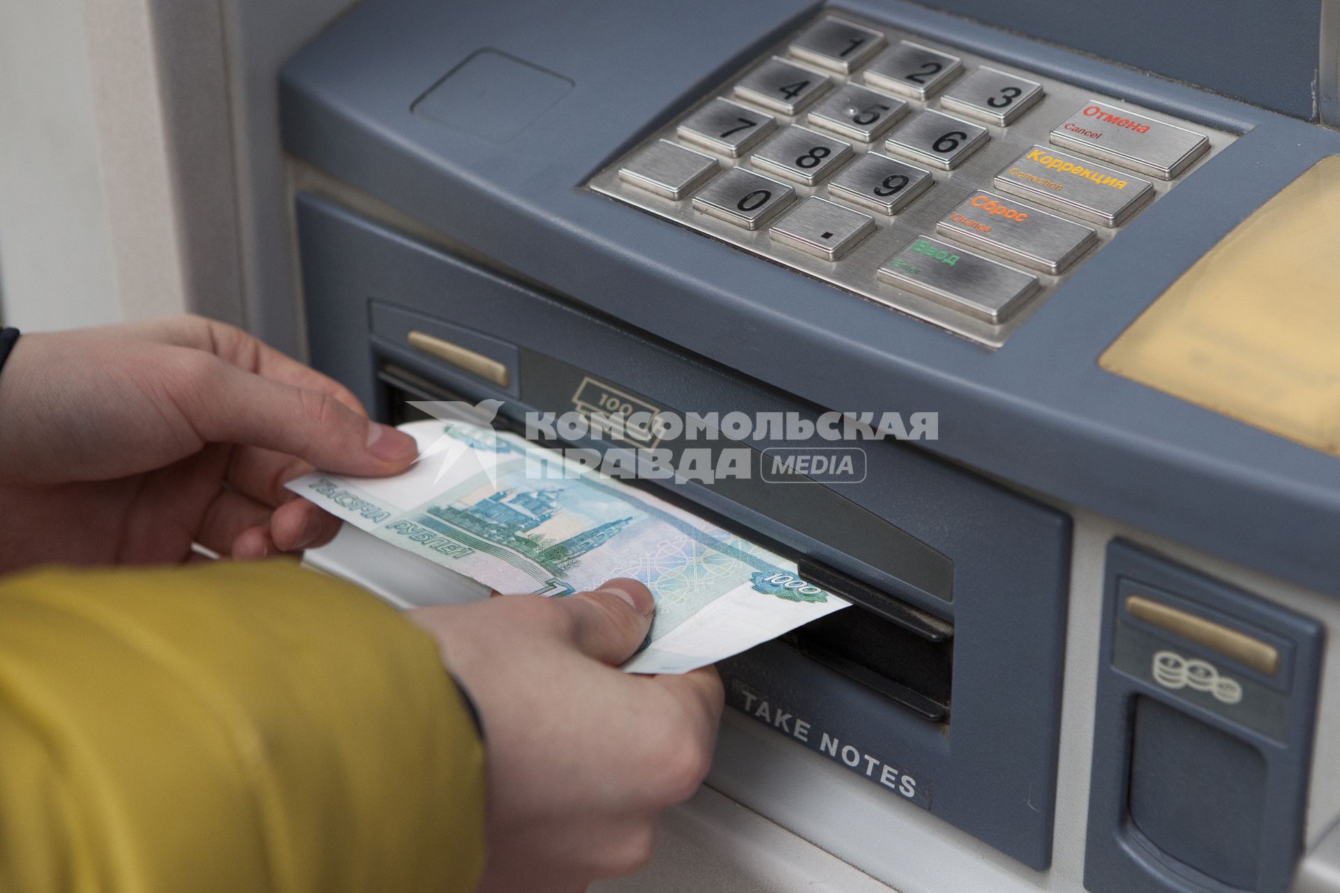 Человек забирает деньги из банкомата.