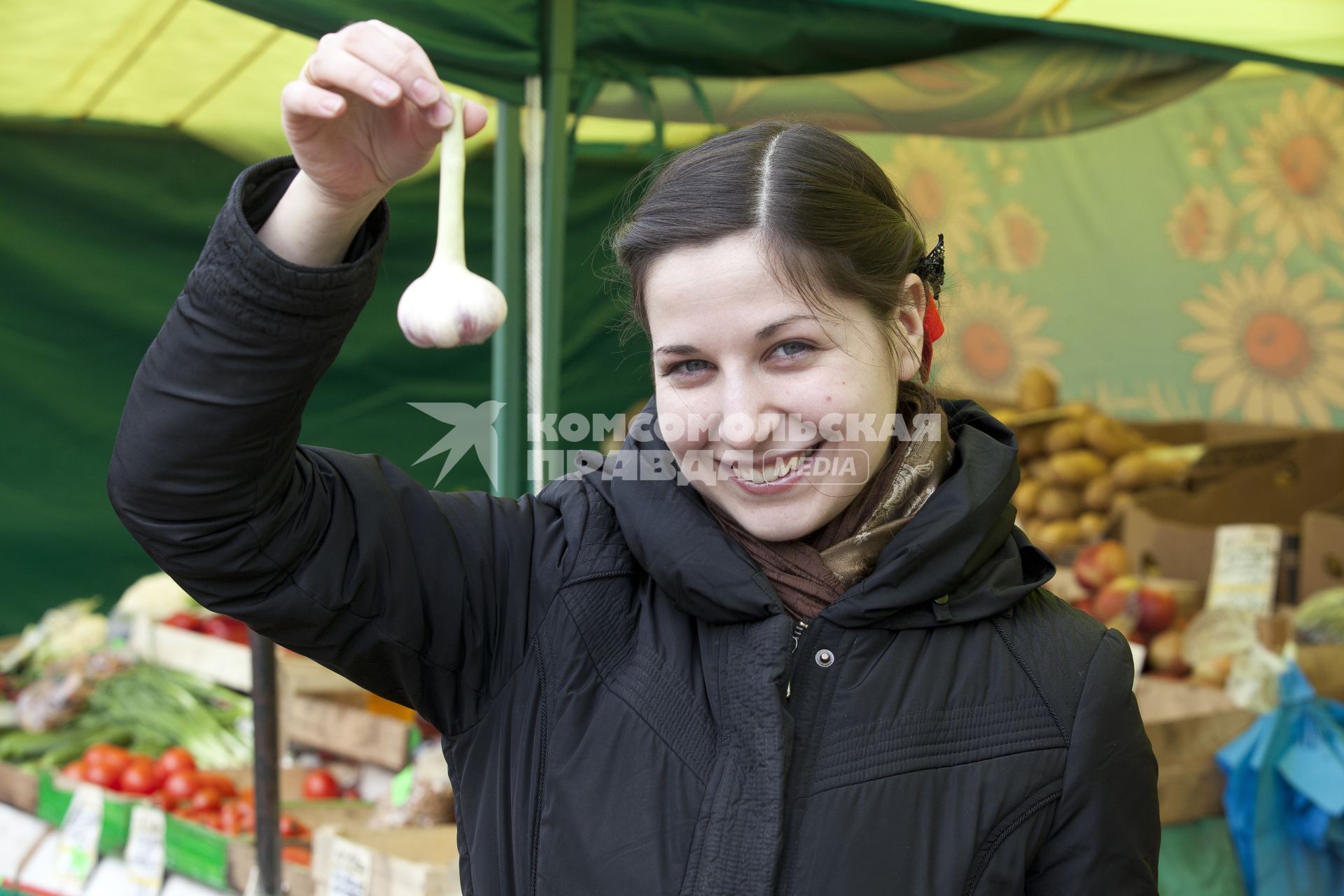 Девушка держит головку чеснока на рынке.