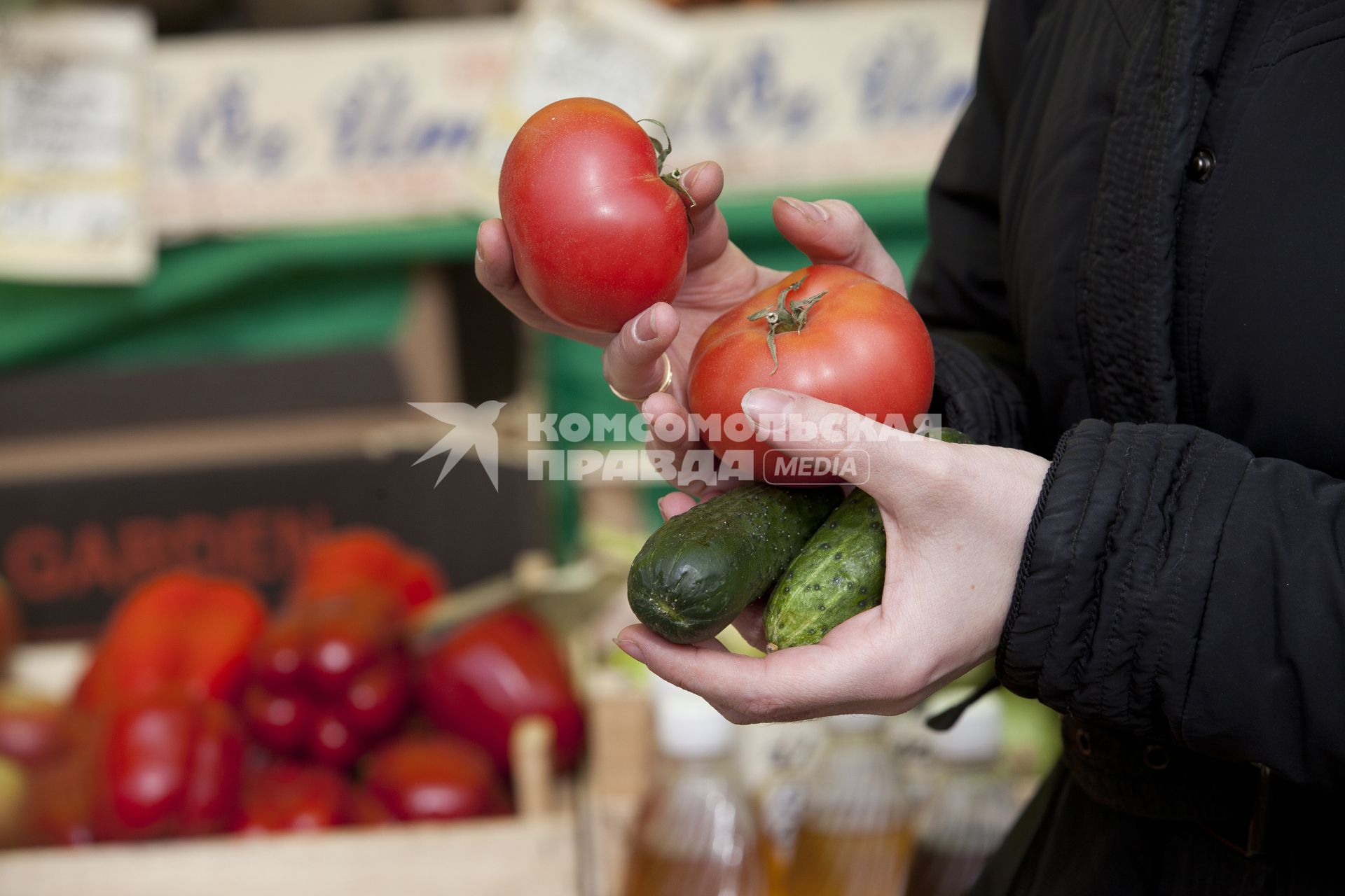 Рука держит помидоры и огурцы на рынке.
