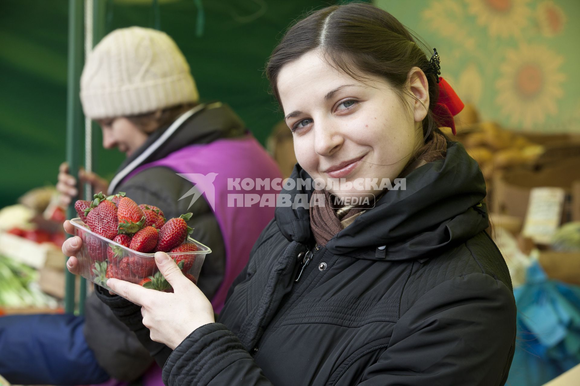 Девушка держит клубнику на рынке.