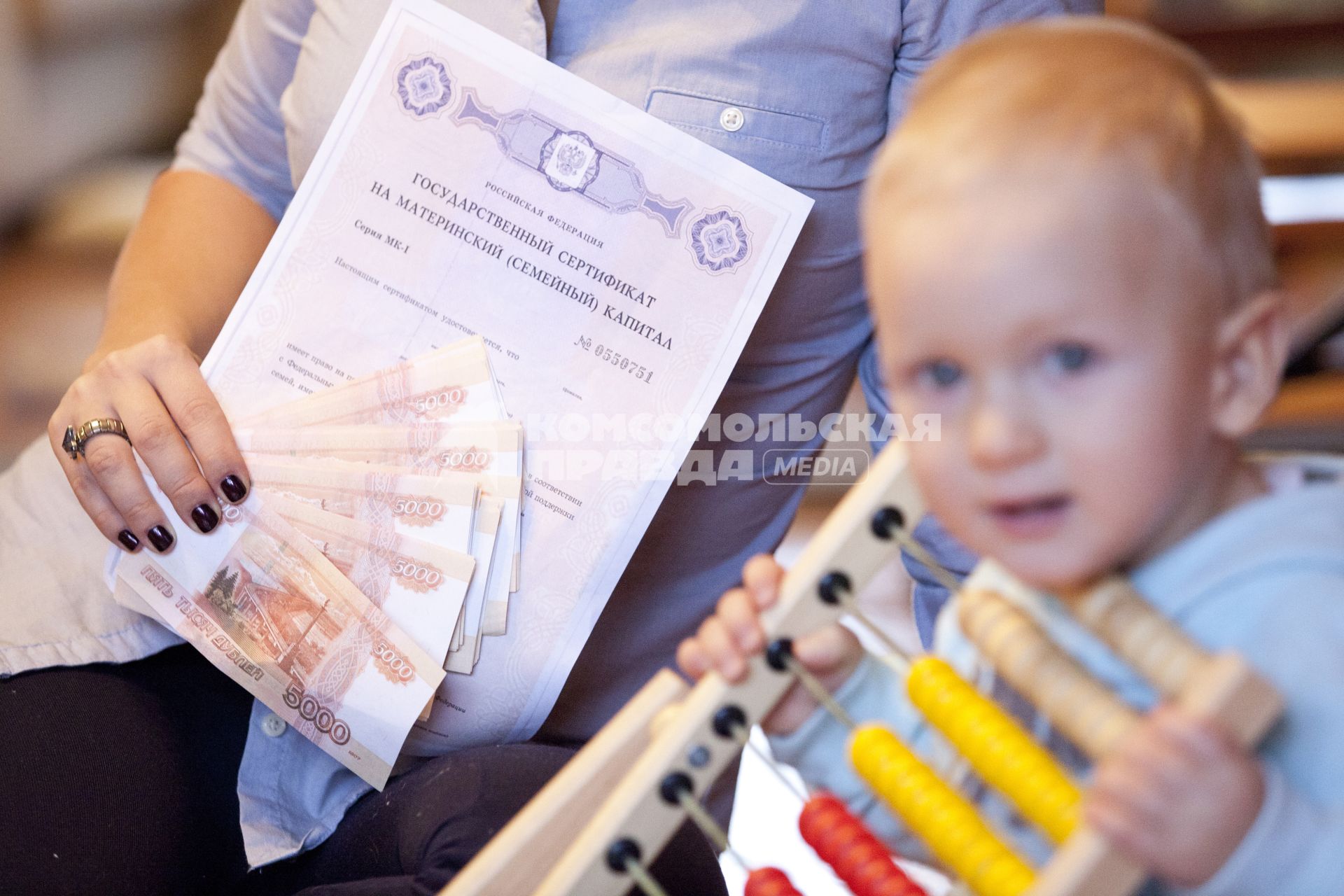 Человек держит деньги и сертификат на материнский капитал на фоне ребенка.