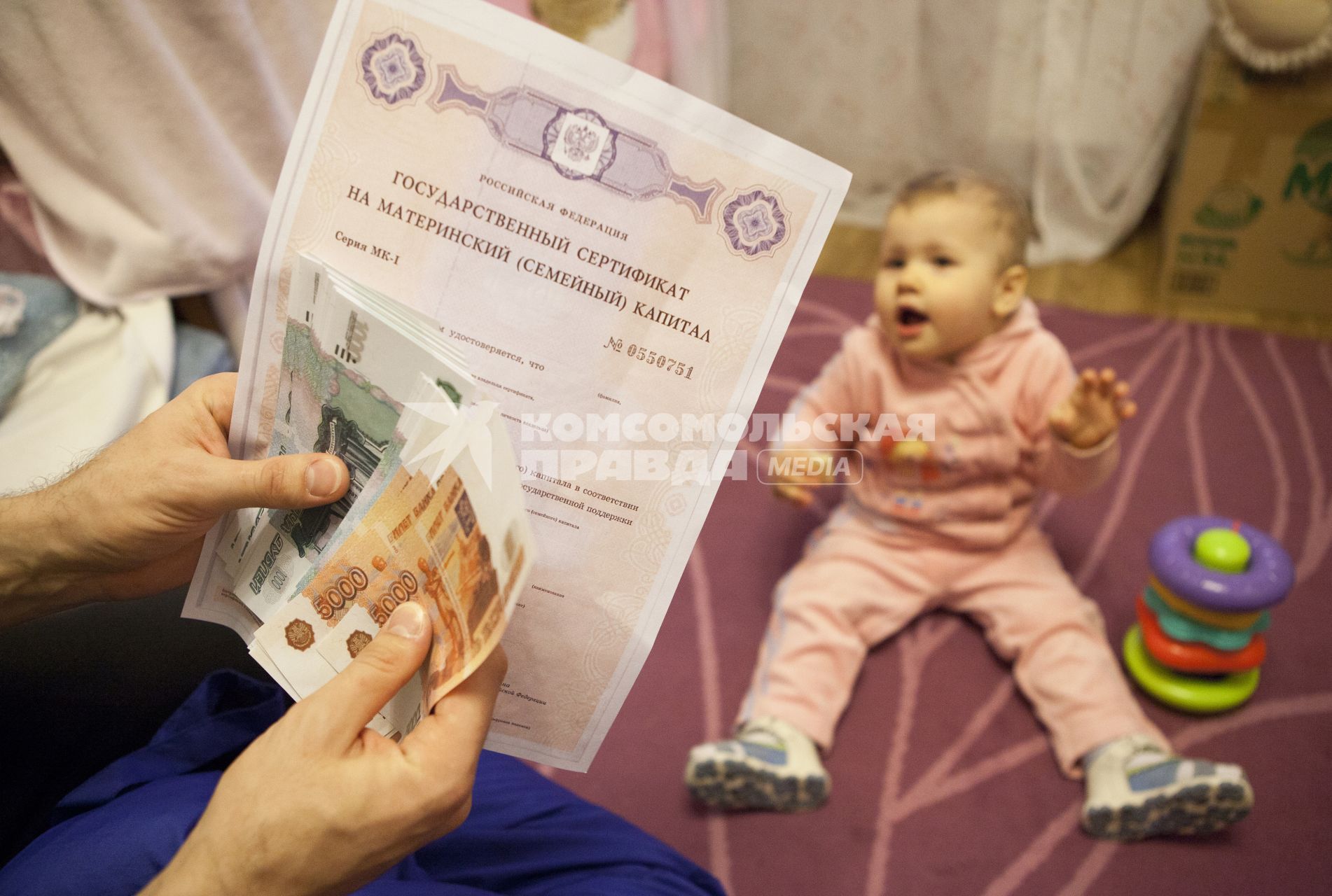 Человек считает деньги и держит сертификат на материнский капитал на фоне ребенка.