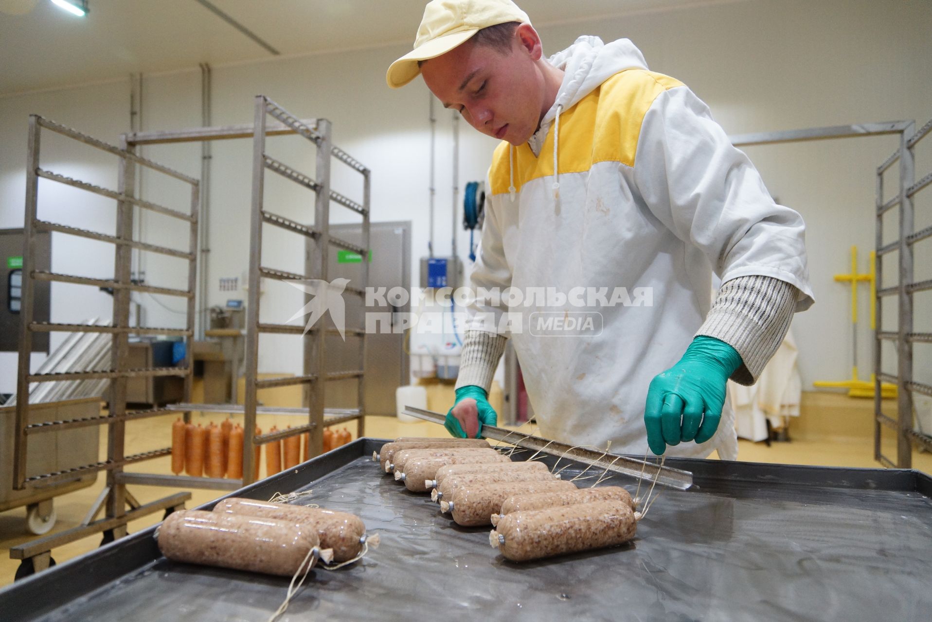 Сотрудник мясокомбината подвешивает упакованную колбасу, для отправки в печь. Агроферма \"Ариант\" в Челябинской области