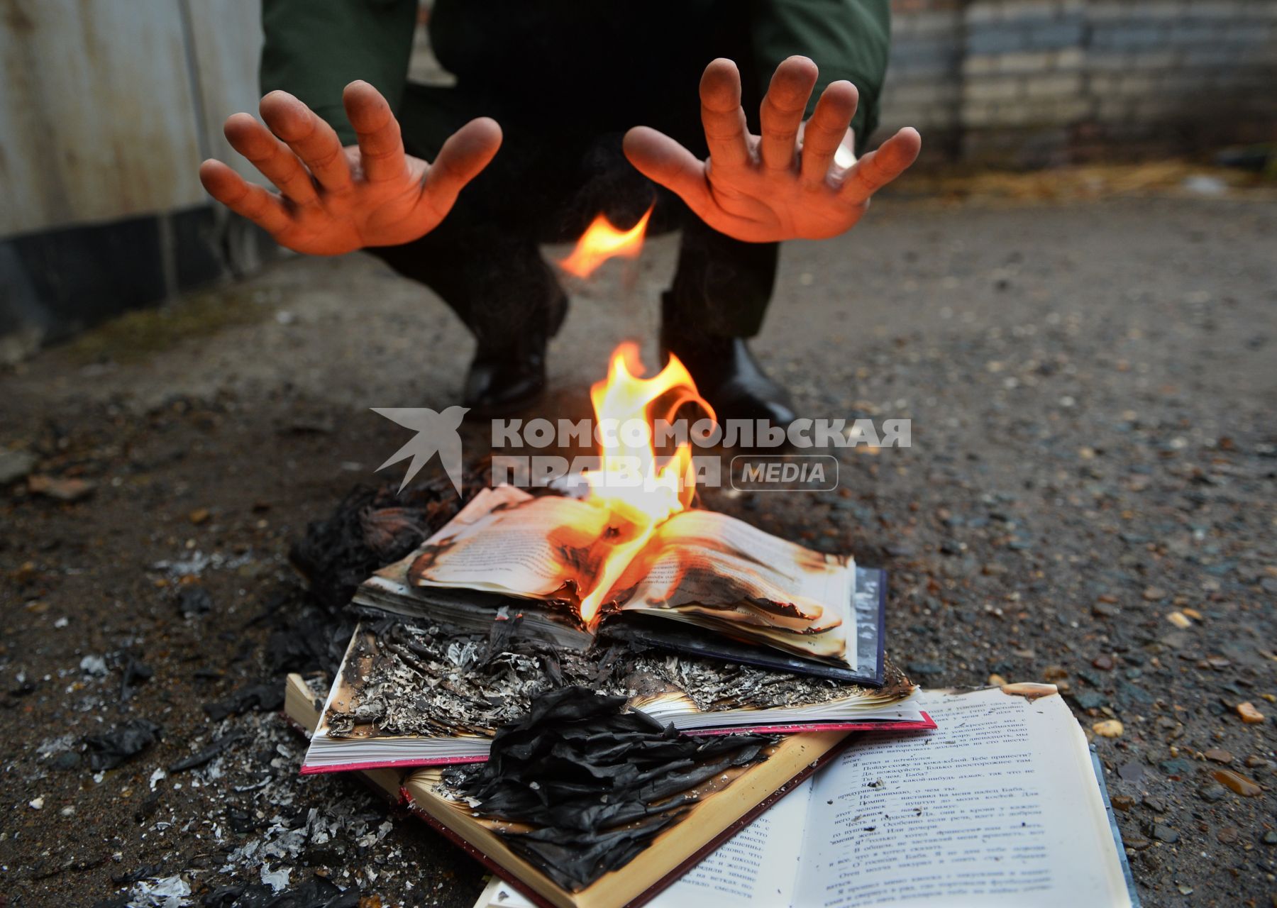 Человек греет руки над горящей книгой