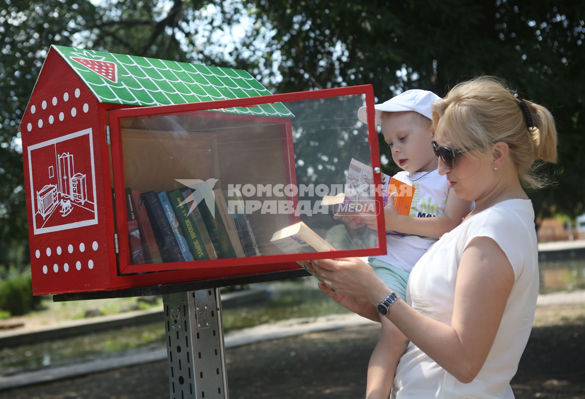 Мама с ребенком выбирает книги в уличной библиотеке организованной в краснодарском парке Городской сад.
