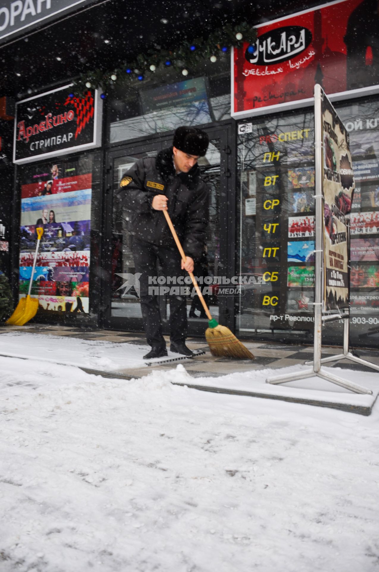 Охранник сметает снег с крыльца стрипбара, кафе и ночного клуба