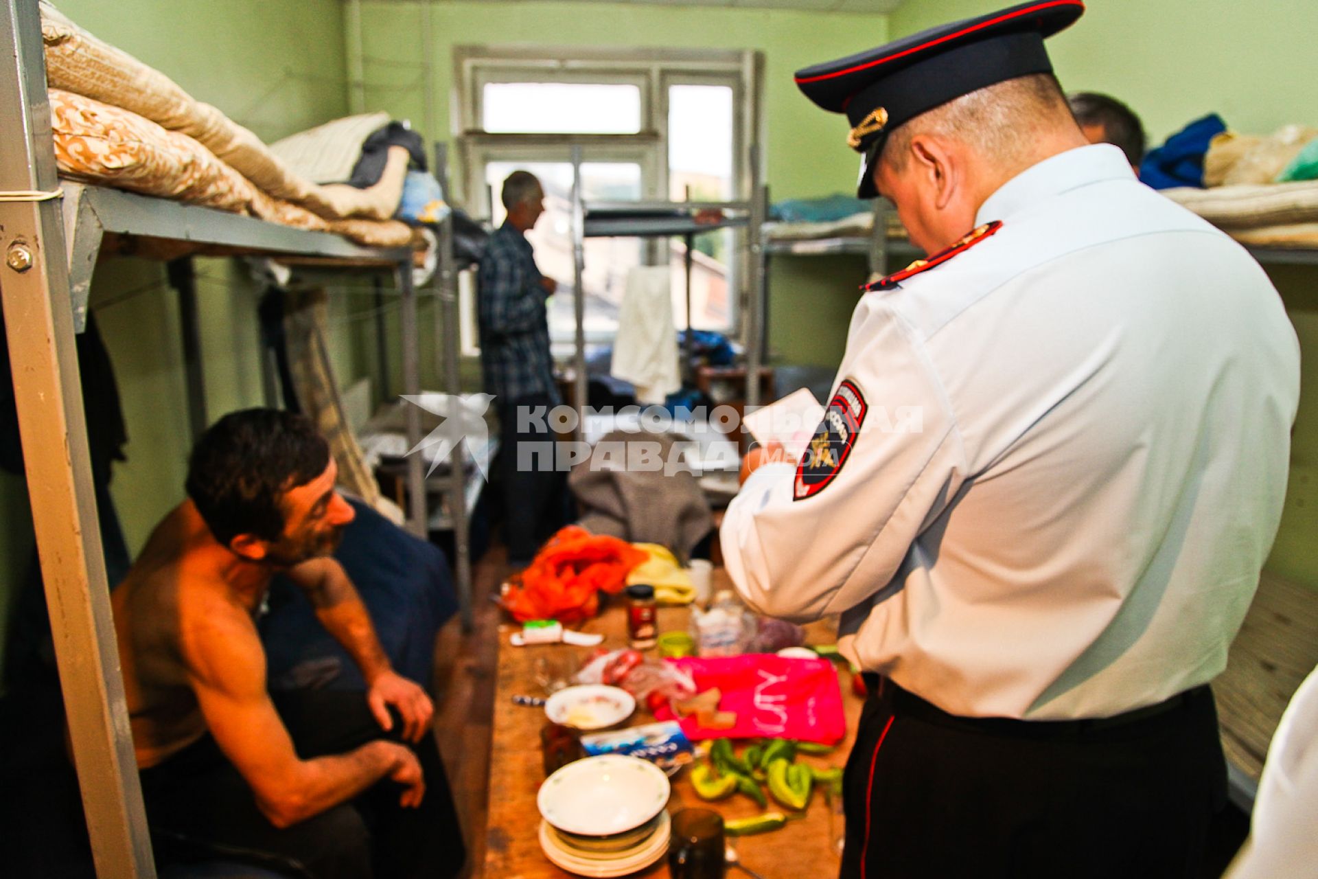 Сотрудник полиции проверяет документы у мужчины в общежитии в рамках рейда УФМС по поиску нелегальных мигрантов