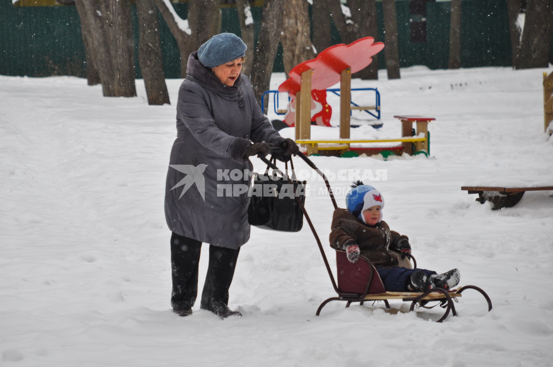 Женщина везет ребенка на санках по снегу