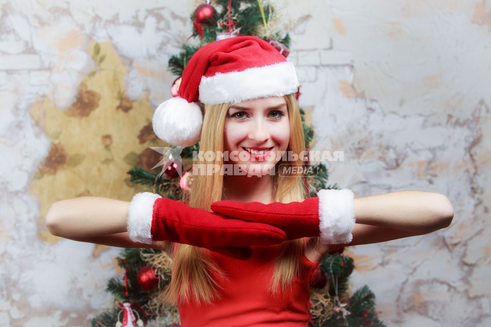 Девушка позирует на камеру на фоне новогодней елки. Снято в студии.