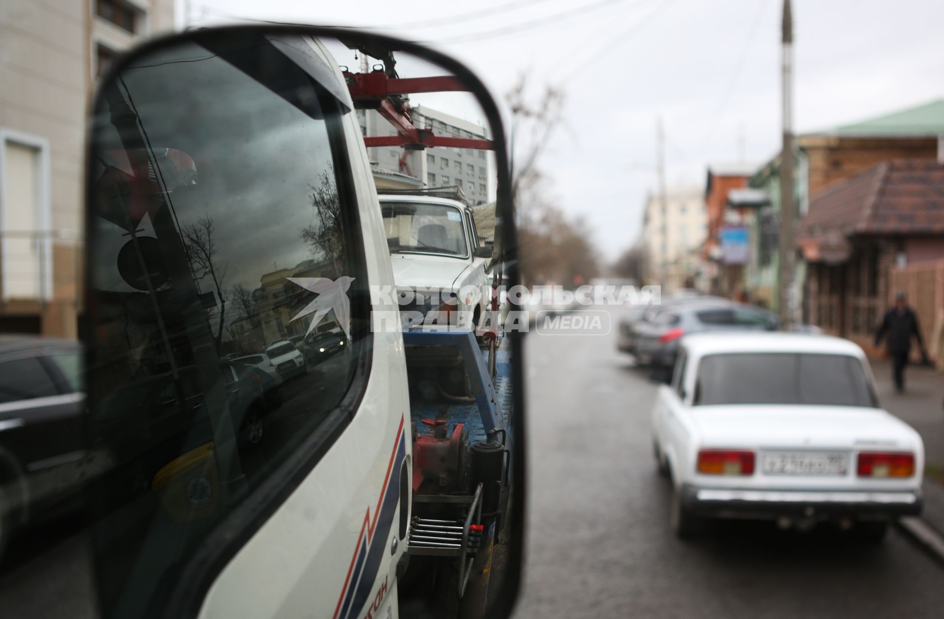 Вид в зеркале эвакуатора, который отвозит машину на штраф стоянку за неправильную парковку.