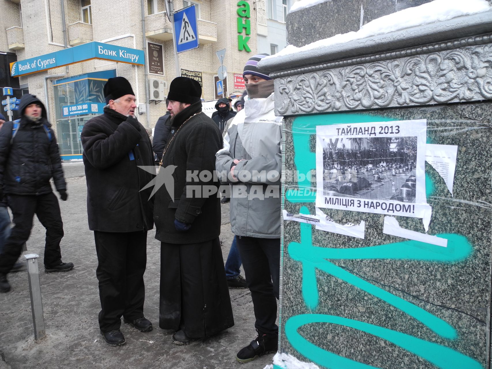 Киев. Священники разговаривают рядом с плакатом `Таиланд 2013 - милиция с народом!` у площади Независимости.