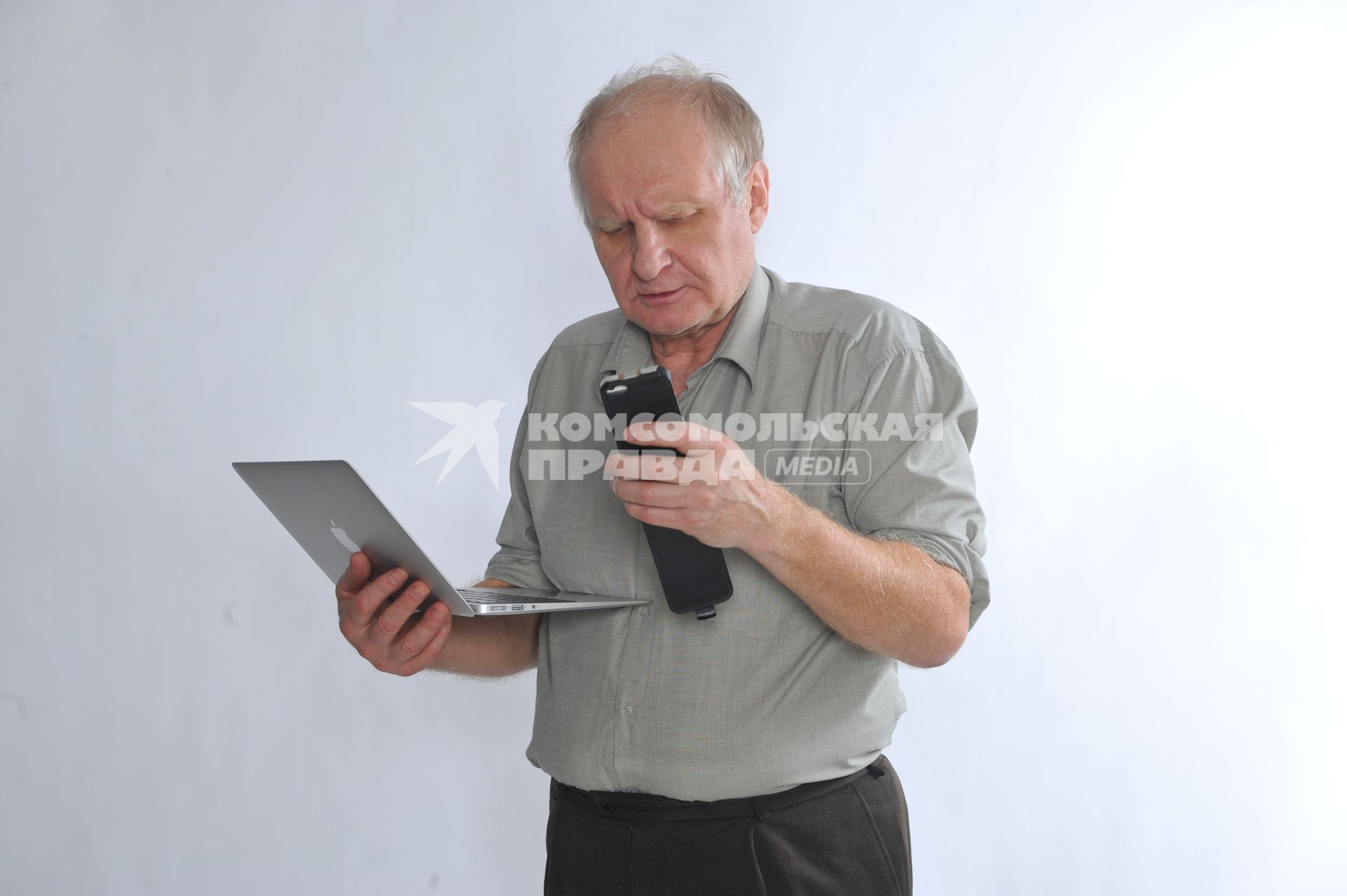 Мужчина держит в руках ноутбук и мобильный телефон.