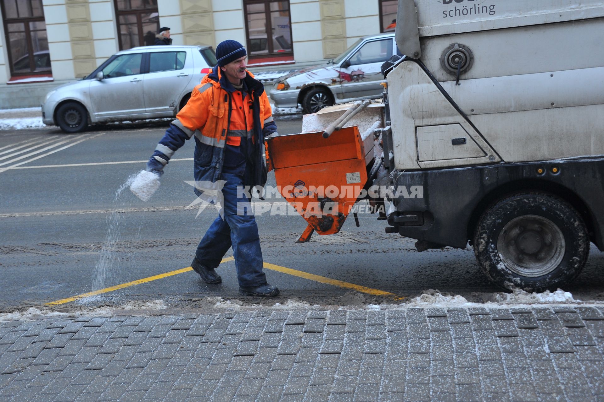 Работник жилищно-коммунального хозяйства посыпает пешеходную зону реагентом.