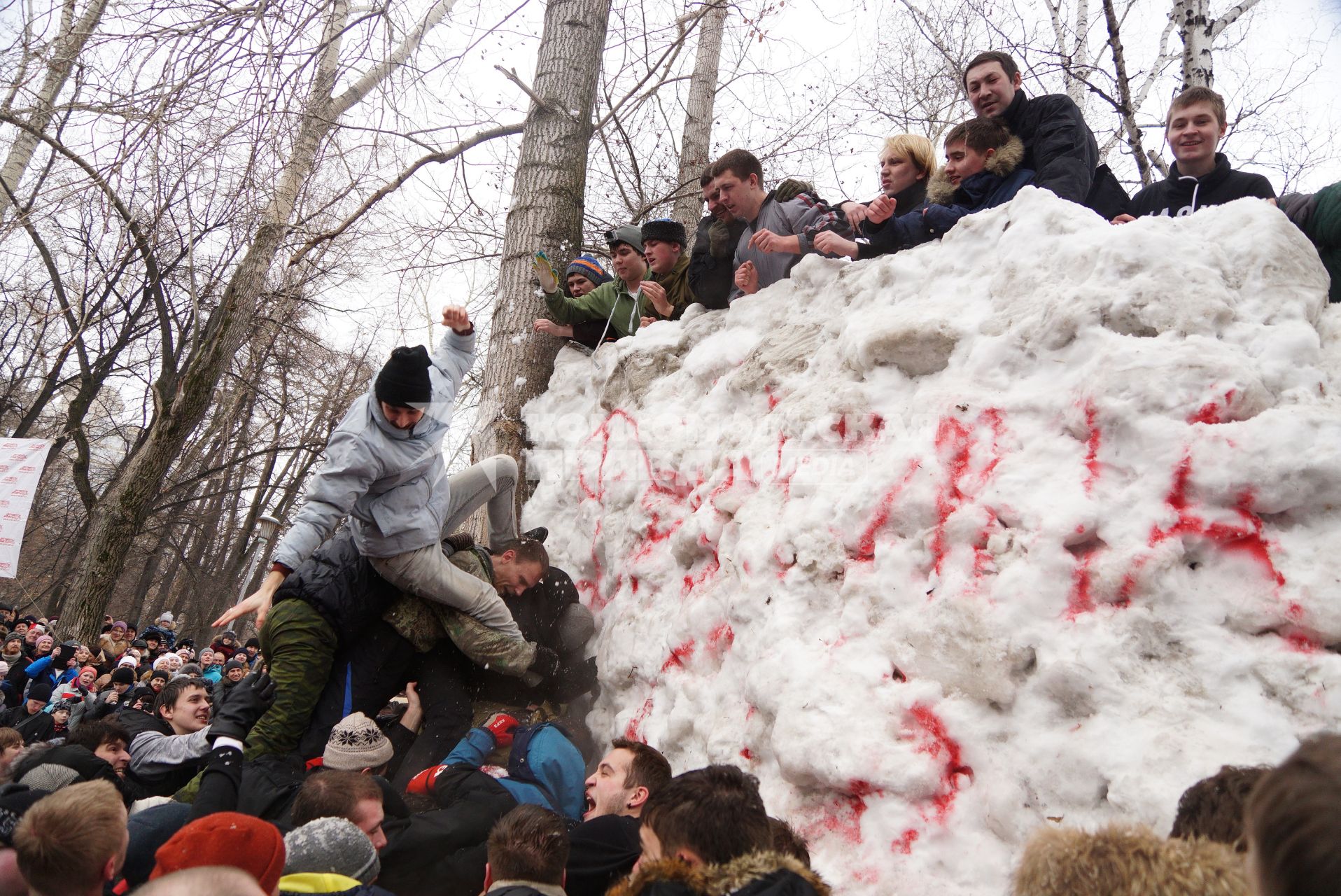 Молодые парни штурмом берут снежную стену. Празднование Масленицы в Харитоновском парке, в Екатеринбурге