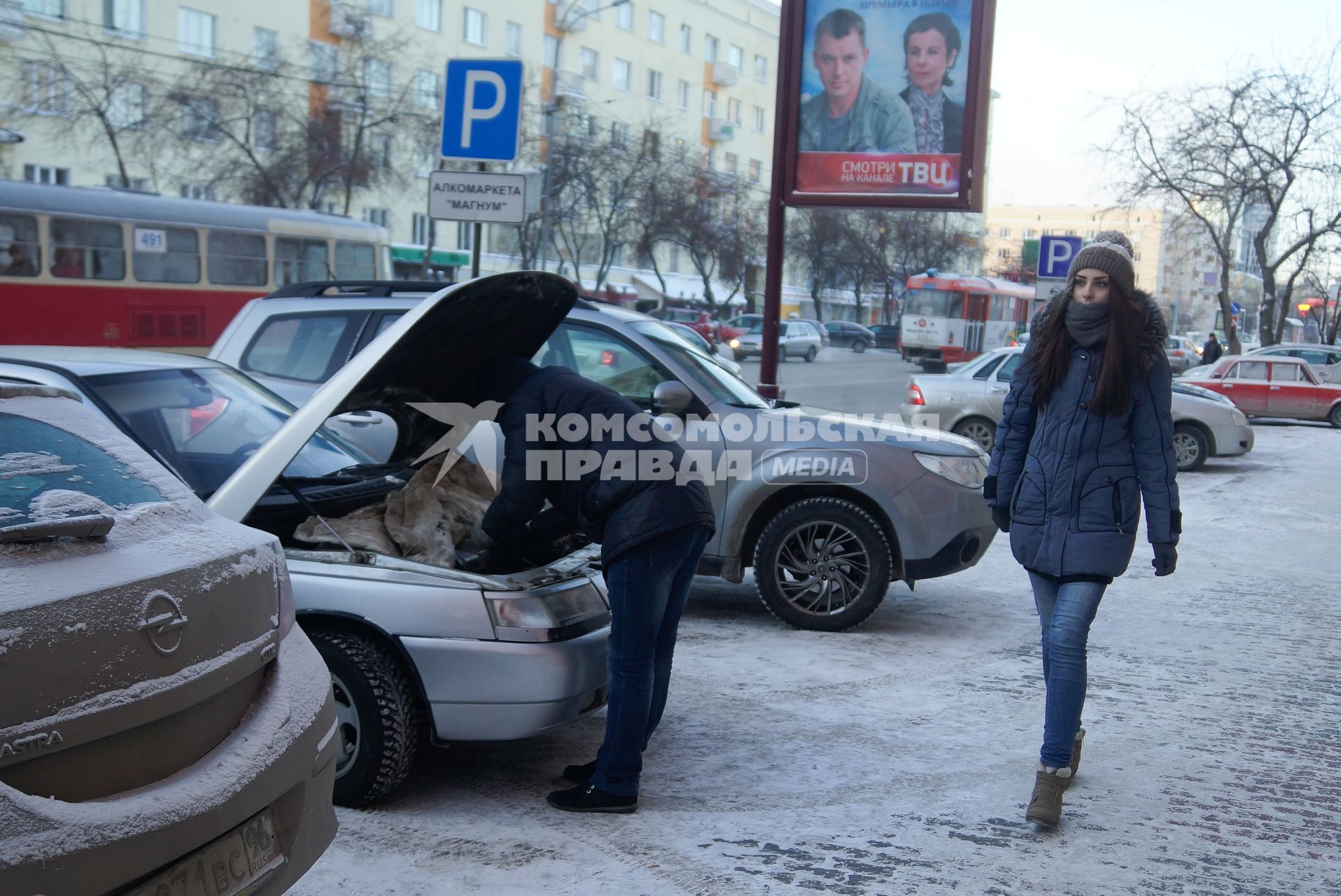 Девушка идет по улице мимо водителя согревающего двигатель автомобиля, во время сильных морозов в Екатеринбурге