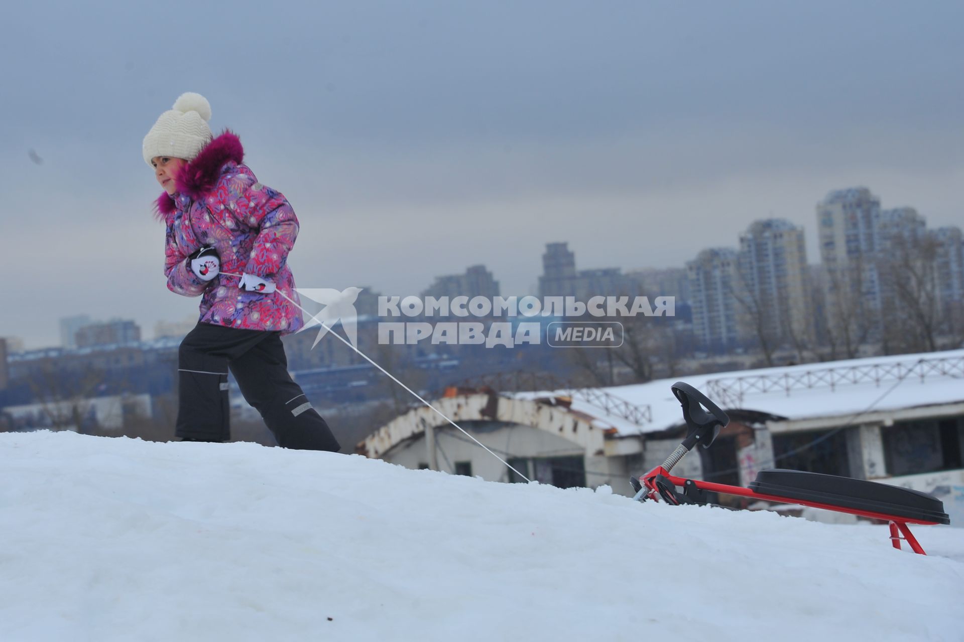 Москва. Девочка с санками поднимается на снежную горку в Парке Победы.