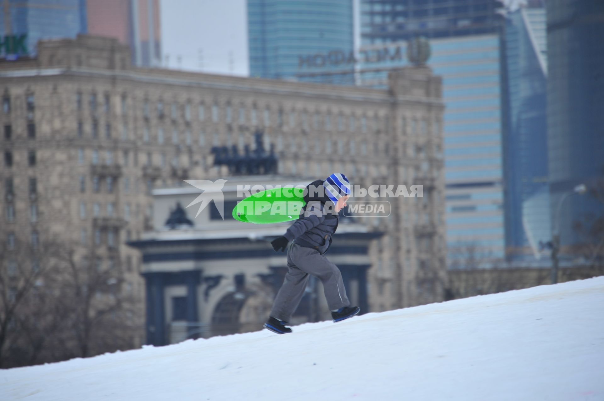 Москва. Мальчик с седушкой для катания поднимается на снежную горку в Парке Победы.