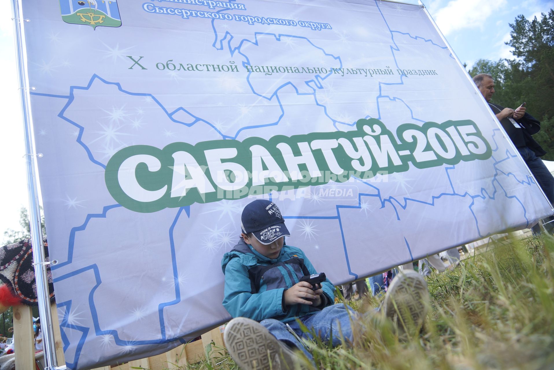 Ребенок сидит у плаката с надписью \"Сабантуй-2015\", во время празднования Сабантуя. село Кадниово. Свердловская область
