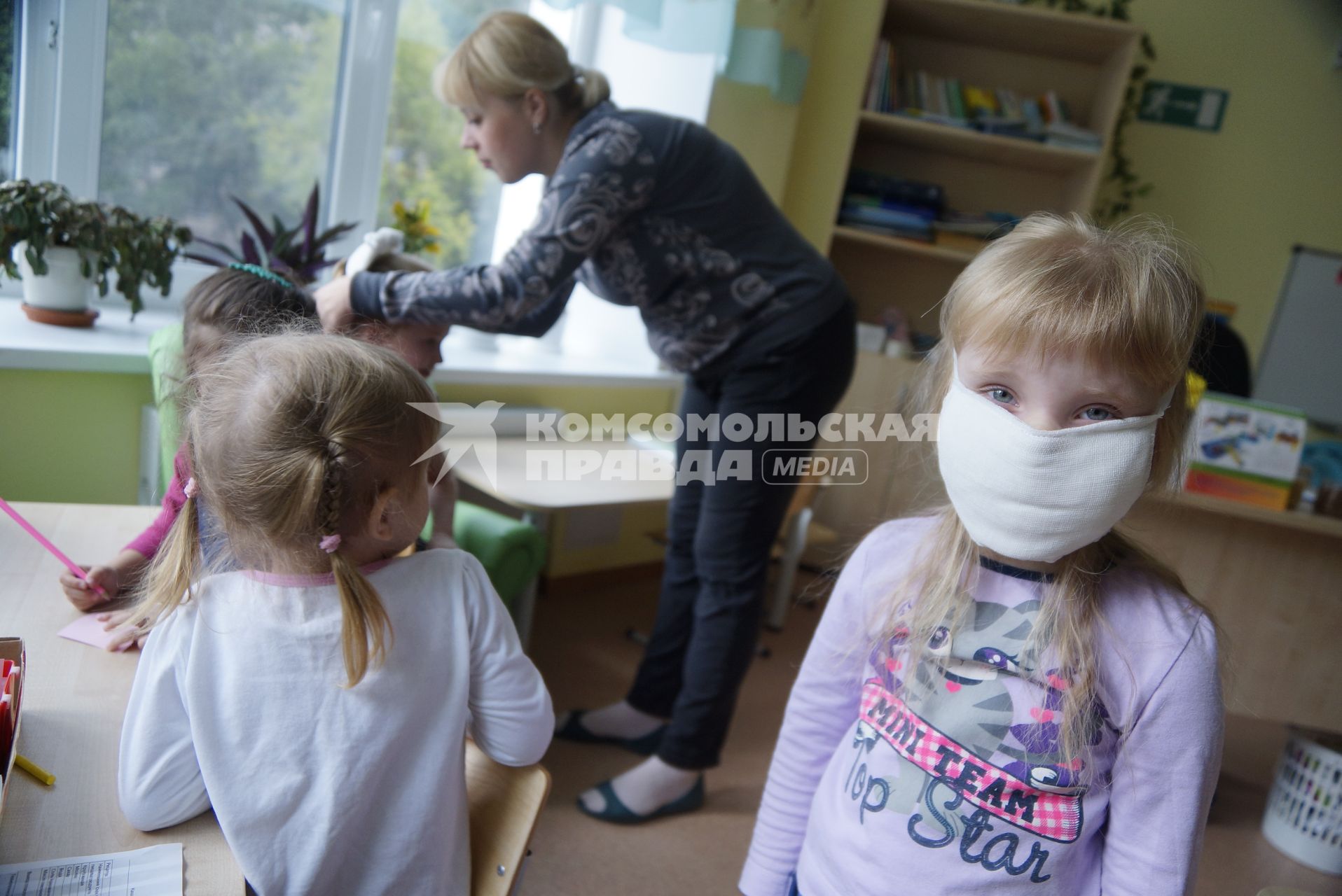 Воспитатель помогает ребенку одеть ватно-марлевую повязку, во время учебной эвакуации из детсого сада при пожаре. Екатеринбург